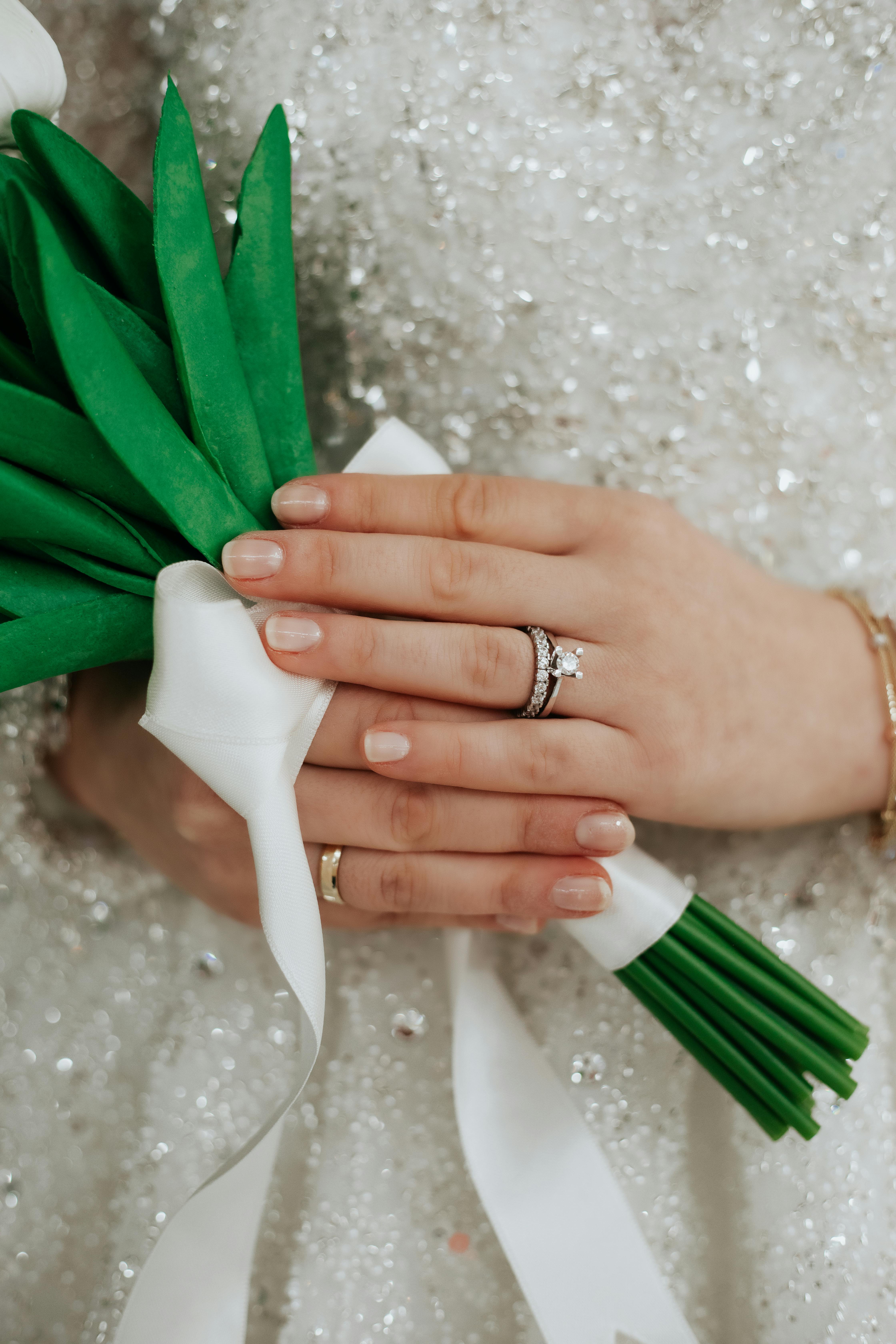 Close-up of a bride's hand holding a green bouquet, showcasing elegant rings.