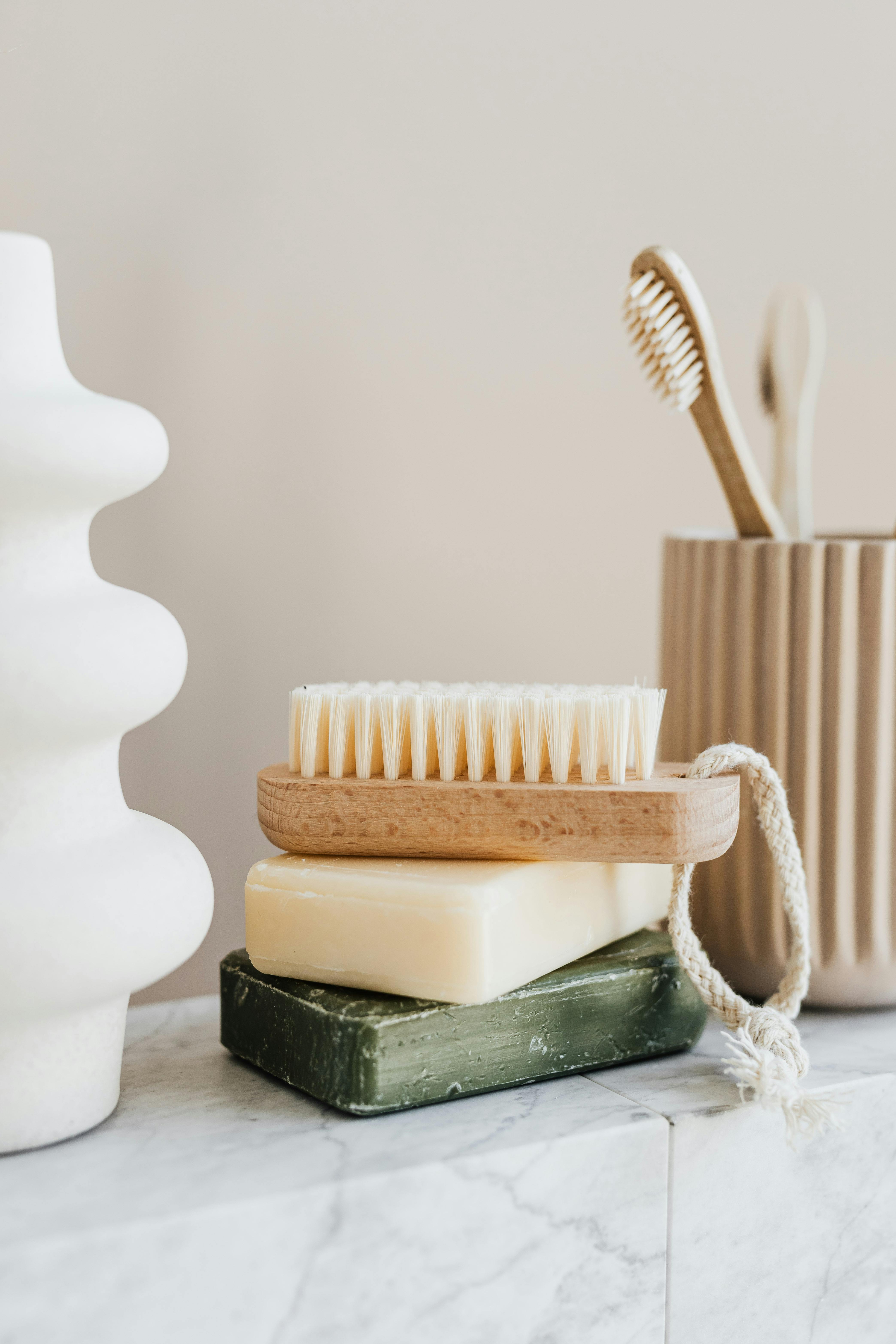Sustainable consumption concept collection of organic cruelty-free soaps with wooden body brush near bamboo sustainable toothbrushes and ceramic white vase on marble tabletop in minimalist bathroom
