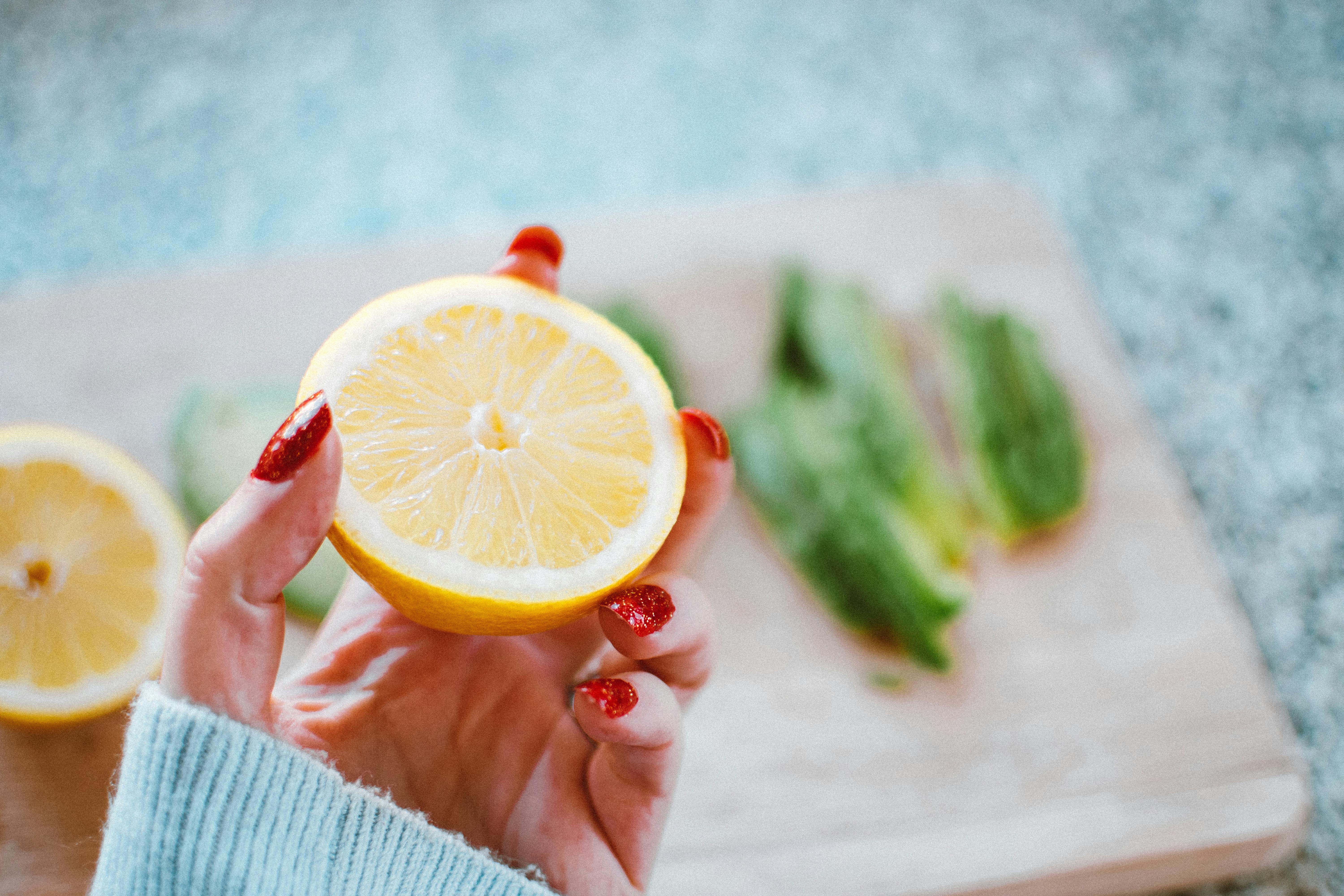 Close-up of a hand with red nails holding a fresh sliced lemon, perfect for culinary or health-themed projects.