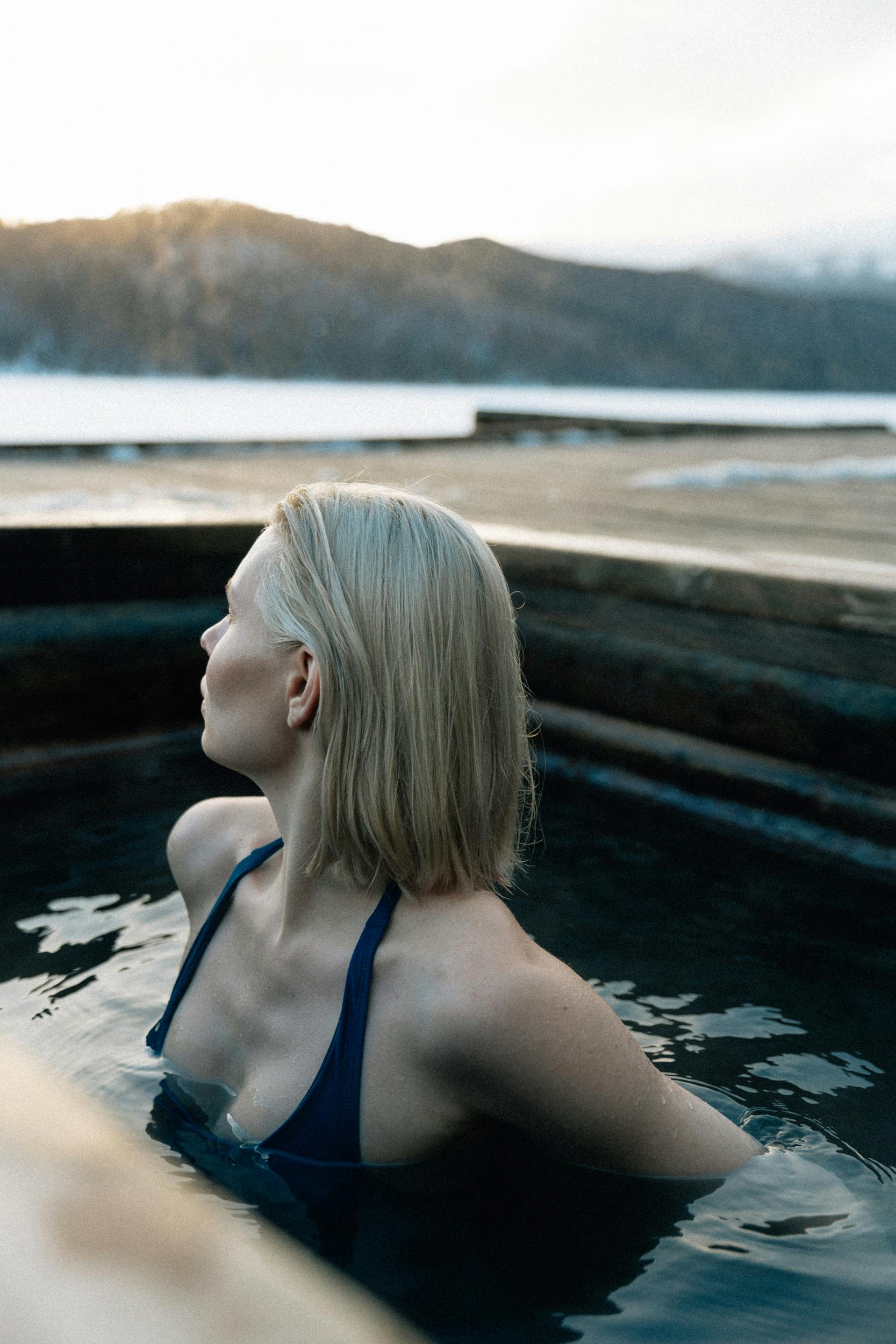 A young woman relaxes in a hot spring during winter with scenic mountain views.
