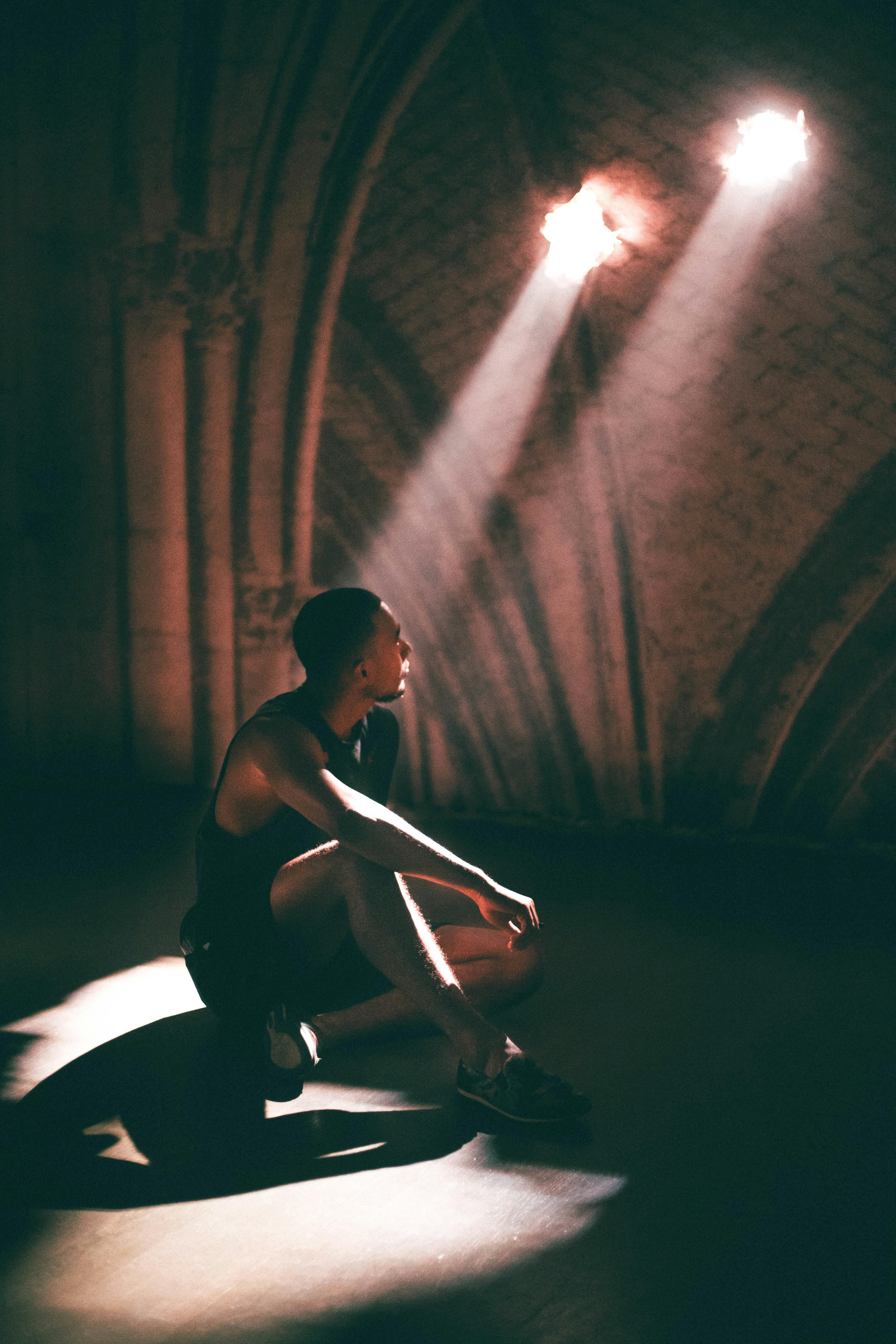 A young man sits in dramatic lighting under spotlight beams in a theater setting.