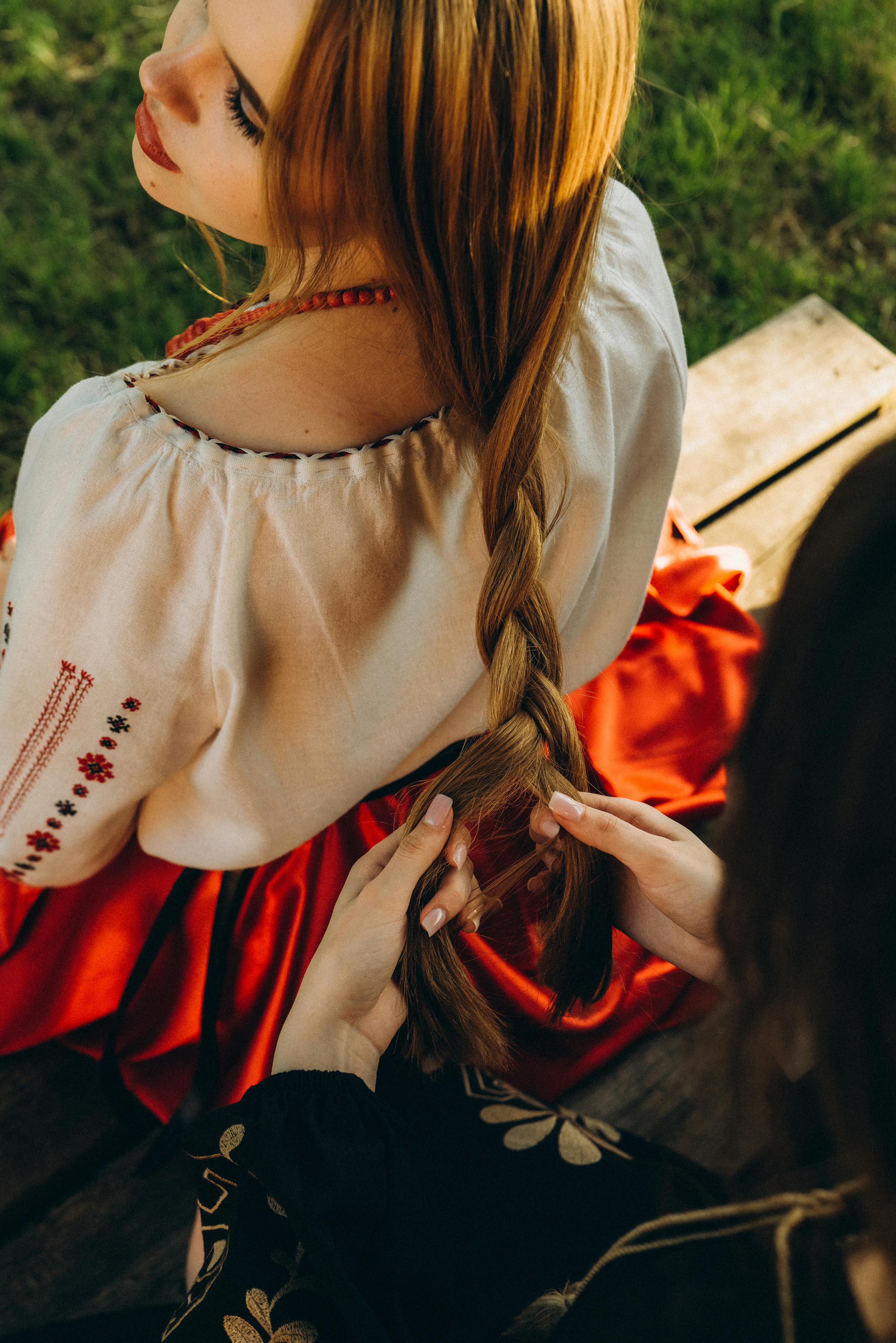 A woman in traditional attire braiding hair outdoors, showcasing cultural heritage.