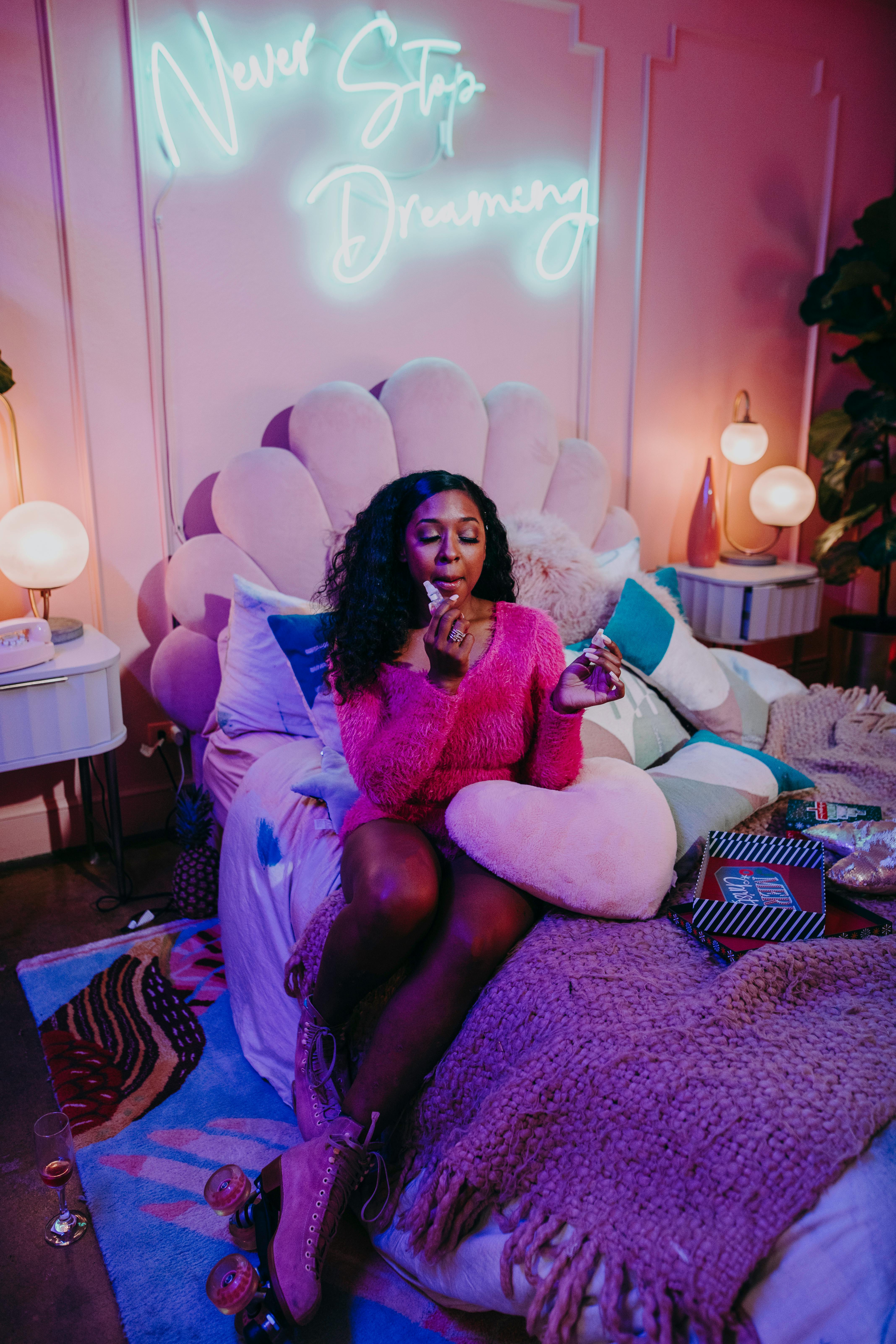 Teen girl in a cozy, stylish bedroom with neon 'Never Stop Dreaming' sign.