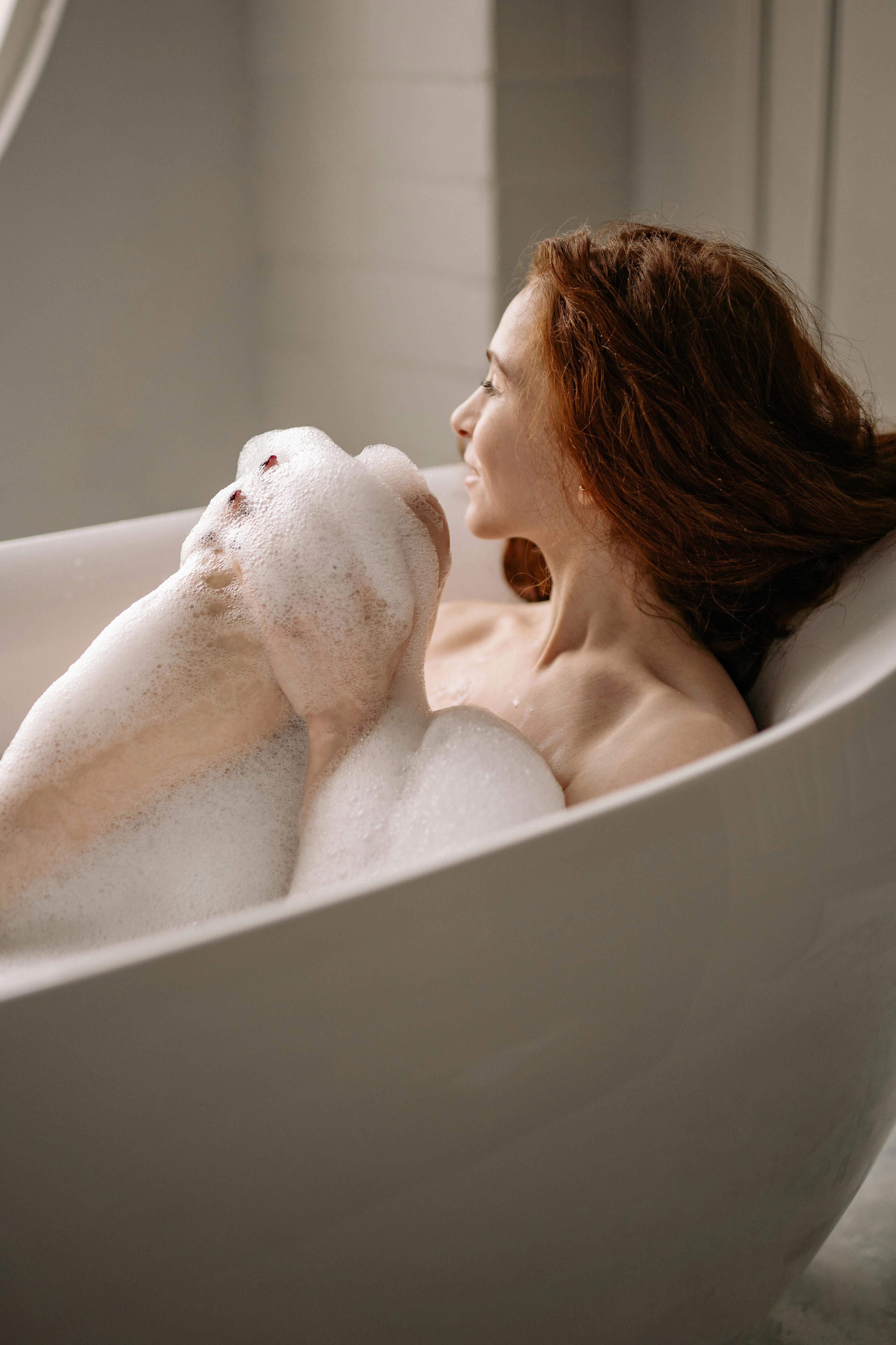 A serene moment of a woman with red hair enjoying a bubble bath indoors, embodying relaxation and self-care.