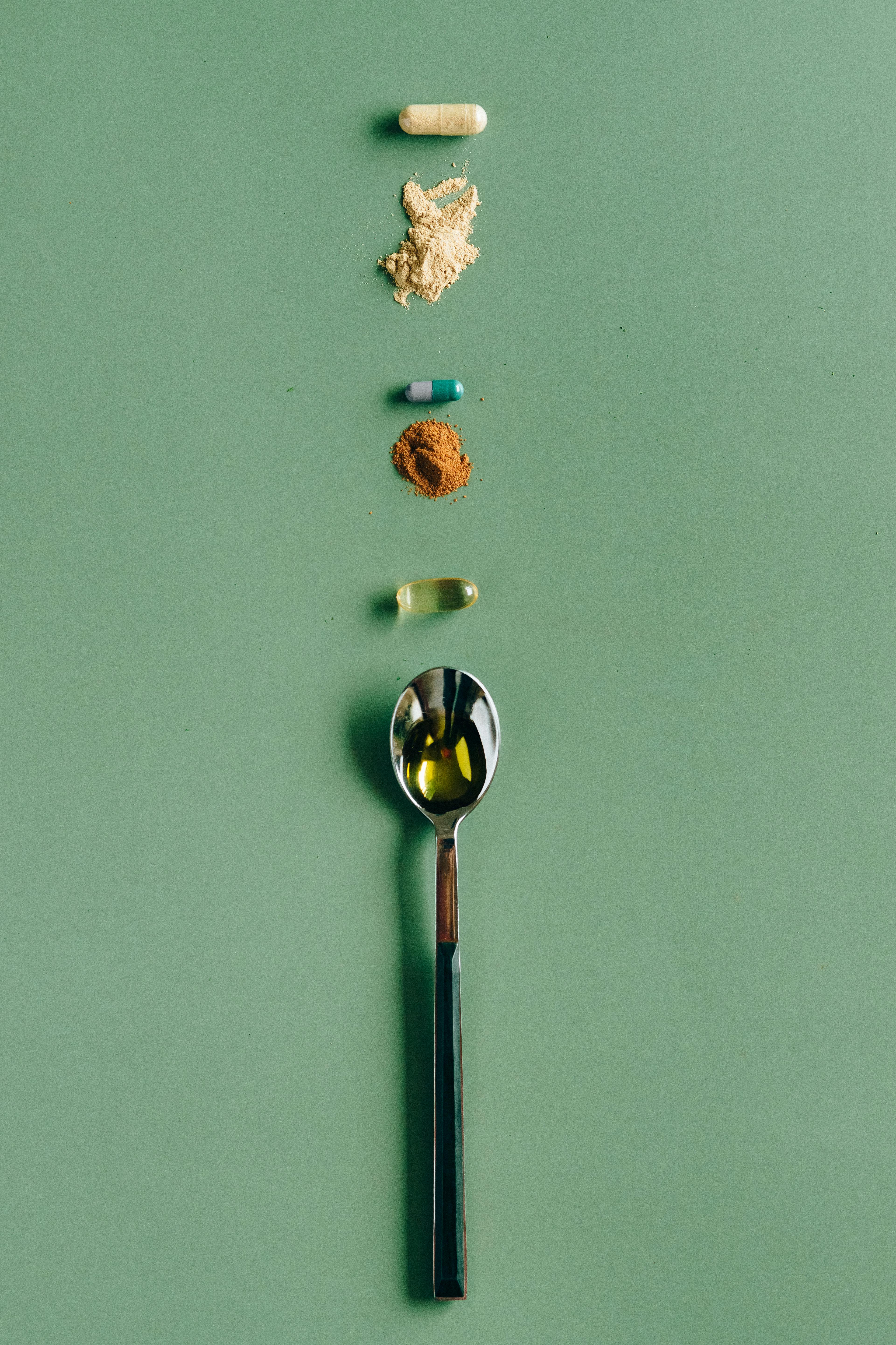 Assorted supplements and a spoon laid out on a green surface, showcasing health concepts.