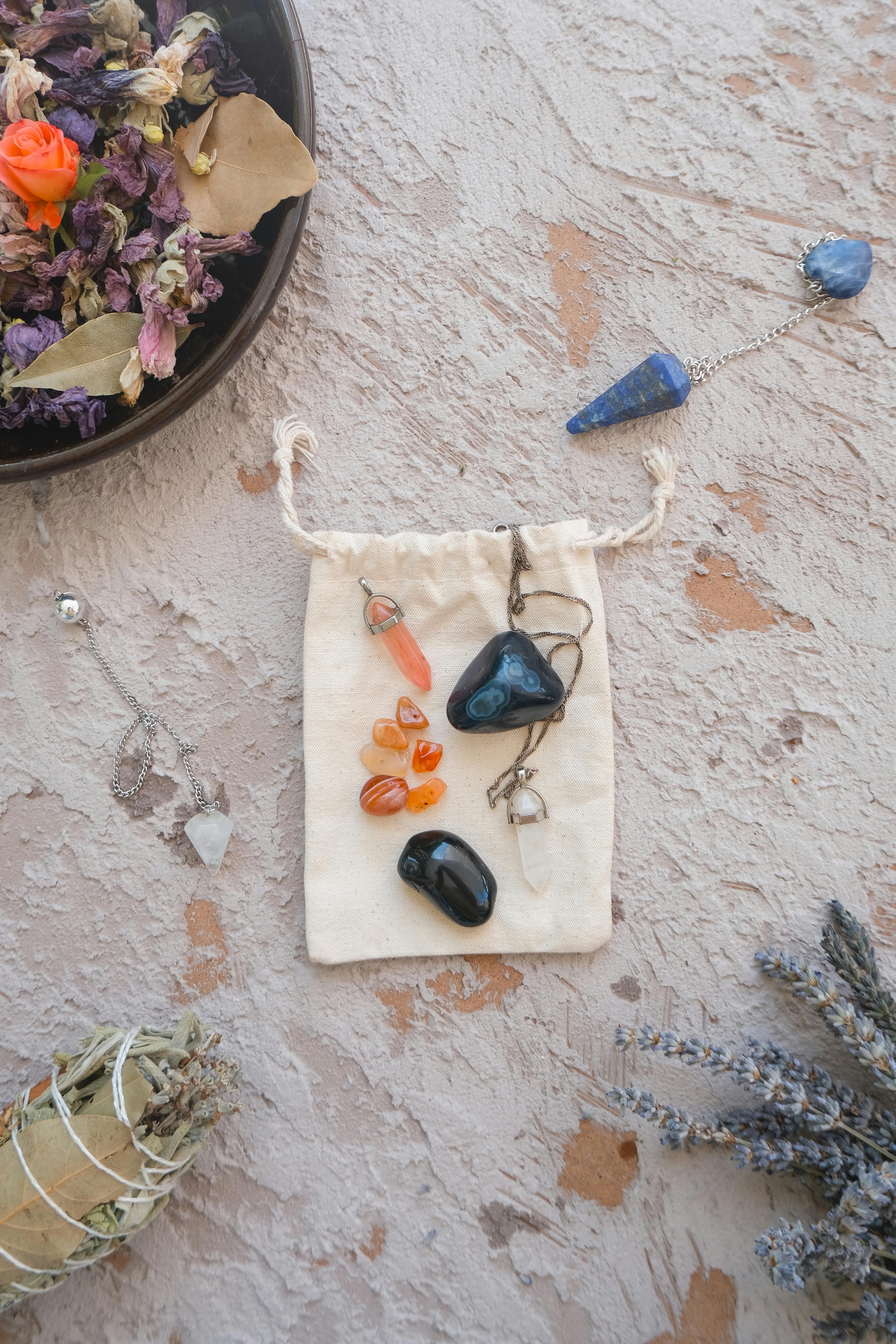 Flat lay of healing crystals, dried flowers, and pendulums for spiritual energy practices.