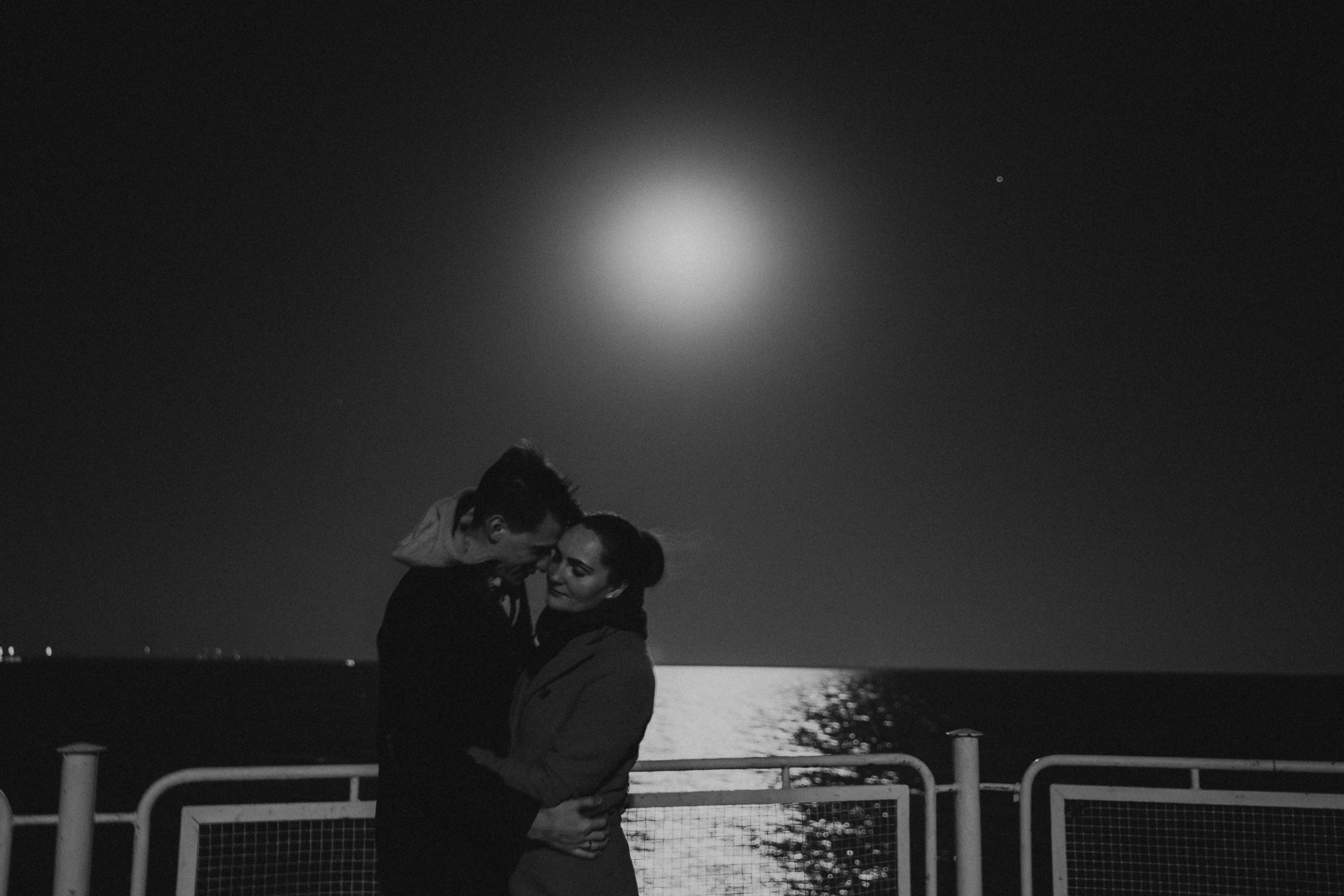 A romantic scene of a couple embracing under the full moon by the water at night.