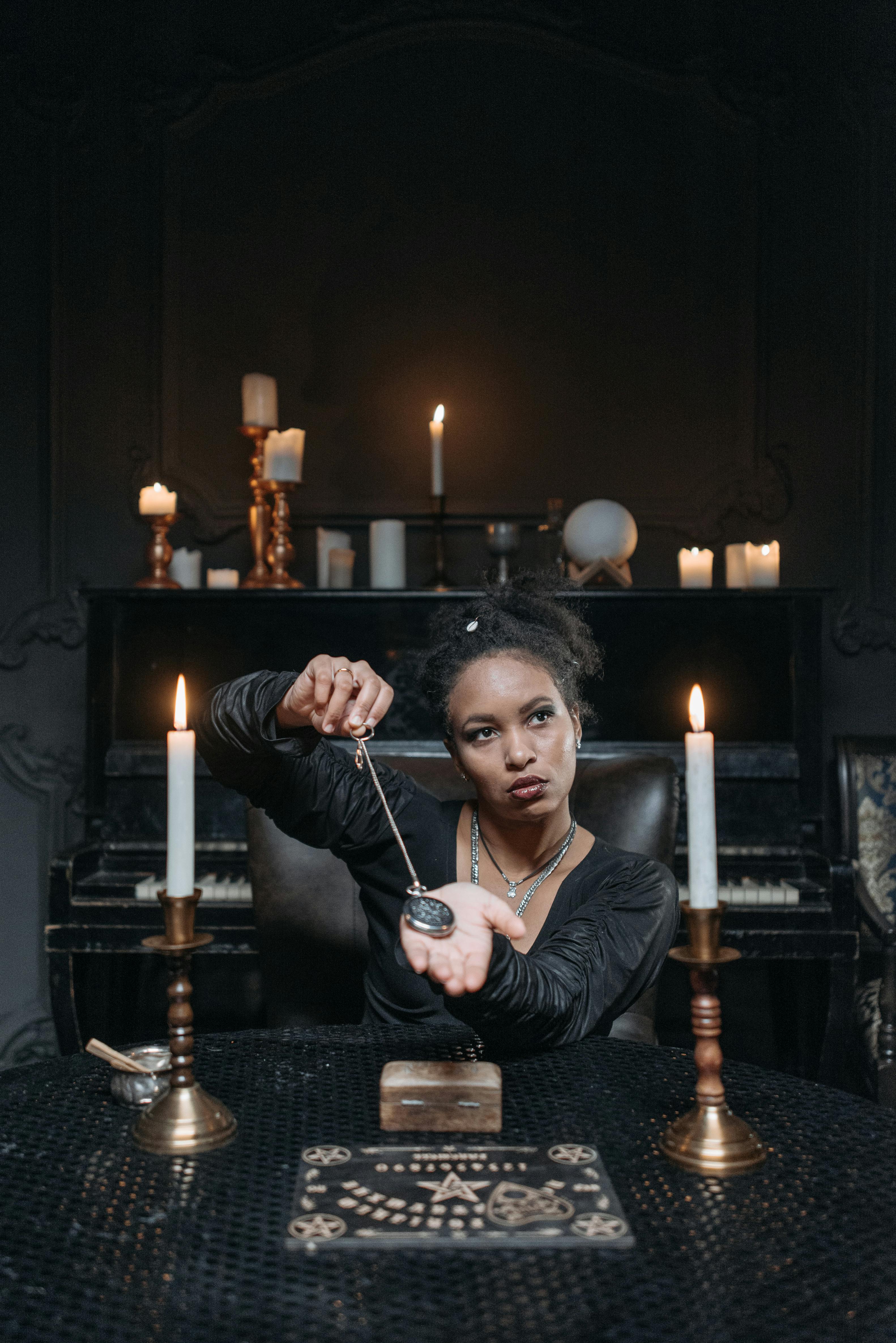 A woman conducting a seance with candles and a pendulum in a mystical setting.