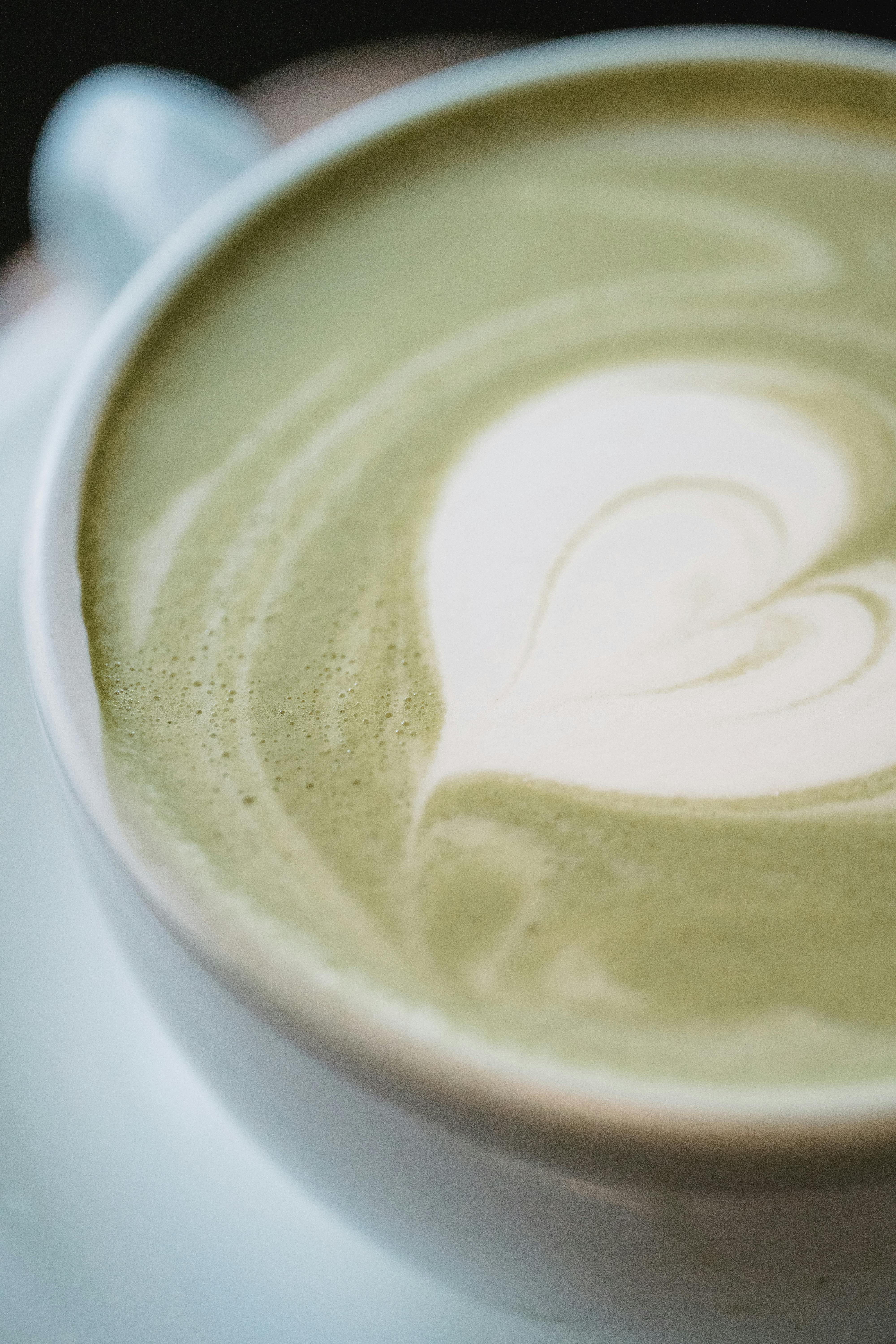 A detailed close-up of a matcha latte with intricate heart-shaped latte art.