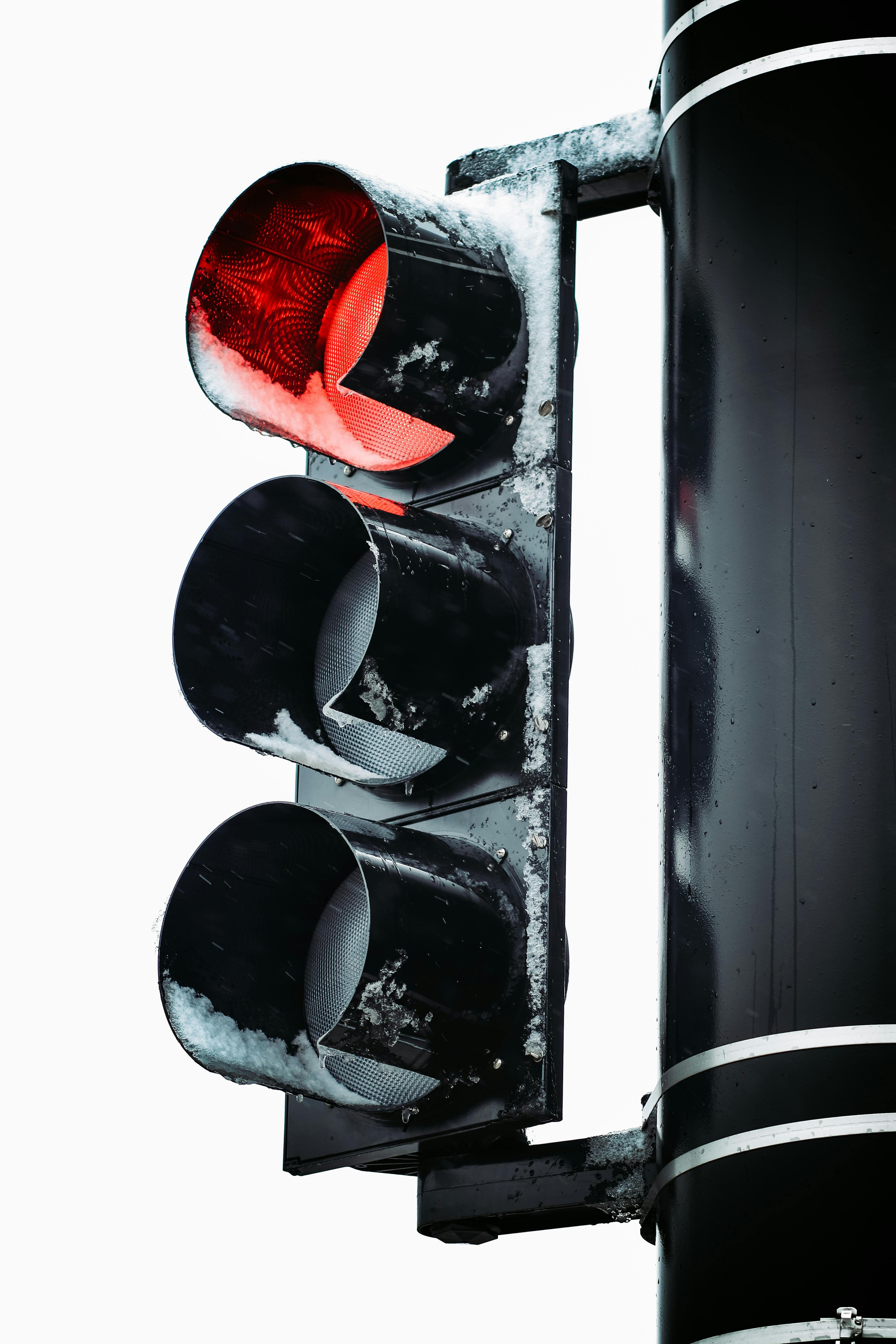 A close-up of a red traffic light covered in snow, against a winter background.