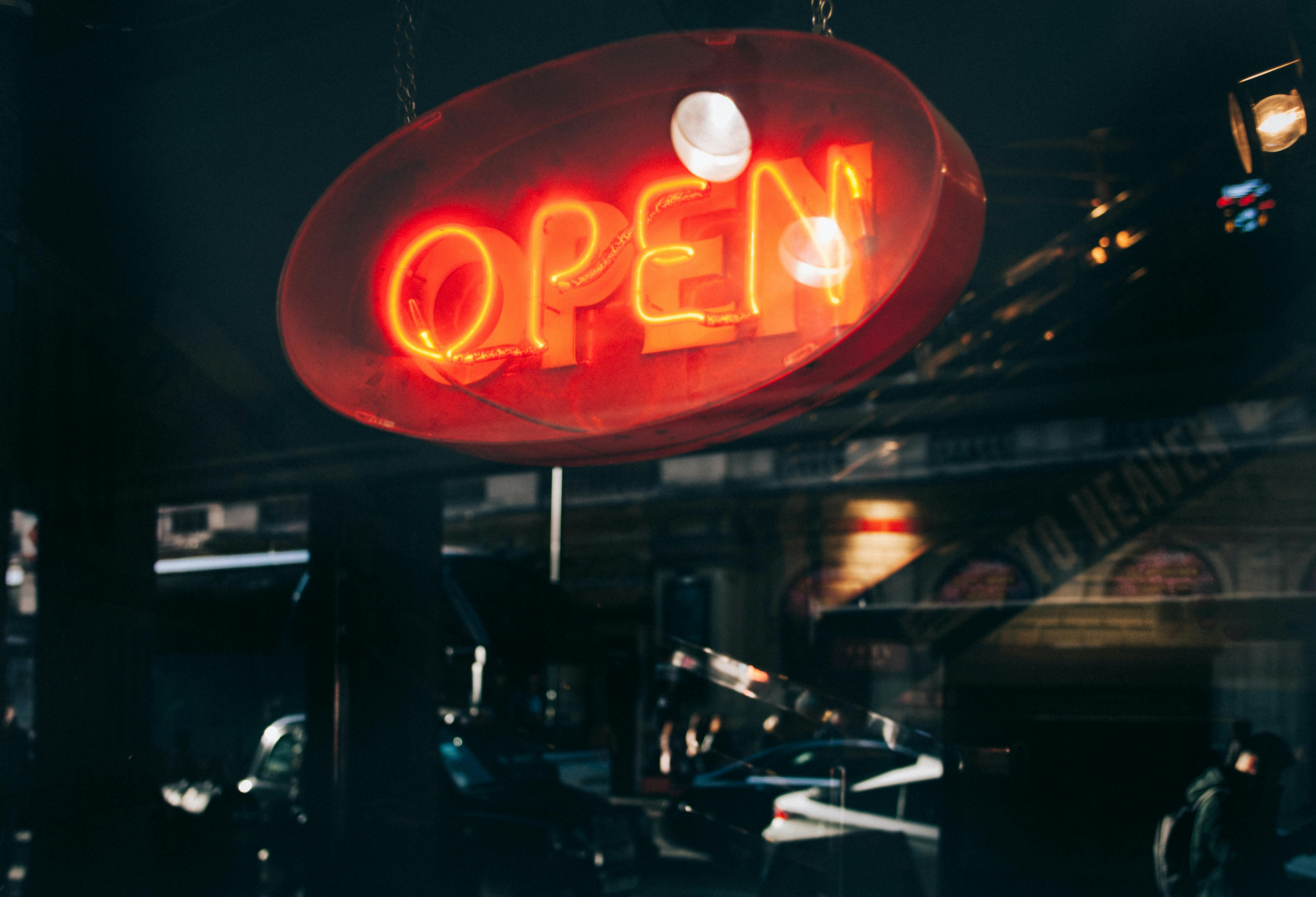 A glowing neon 'OPEN' sign illuminates an evening street scene, reflecting urban nightlife.
