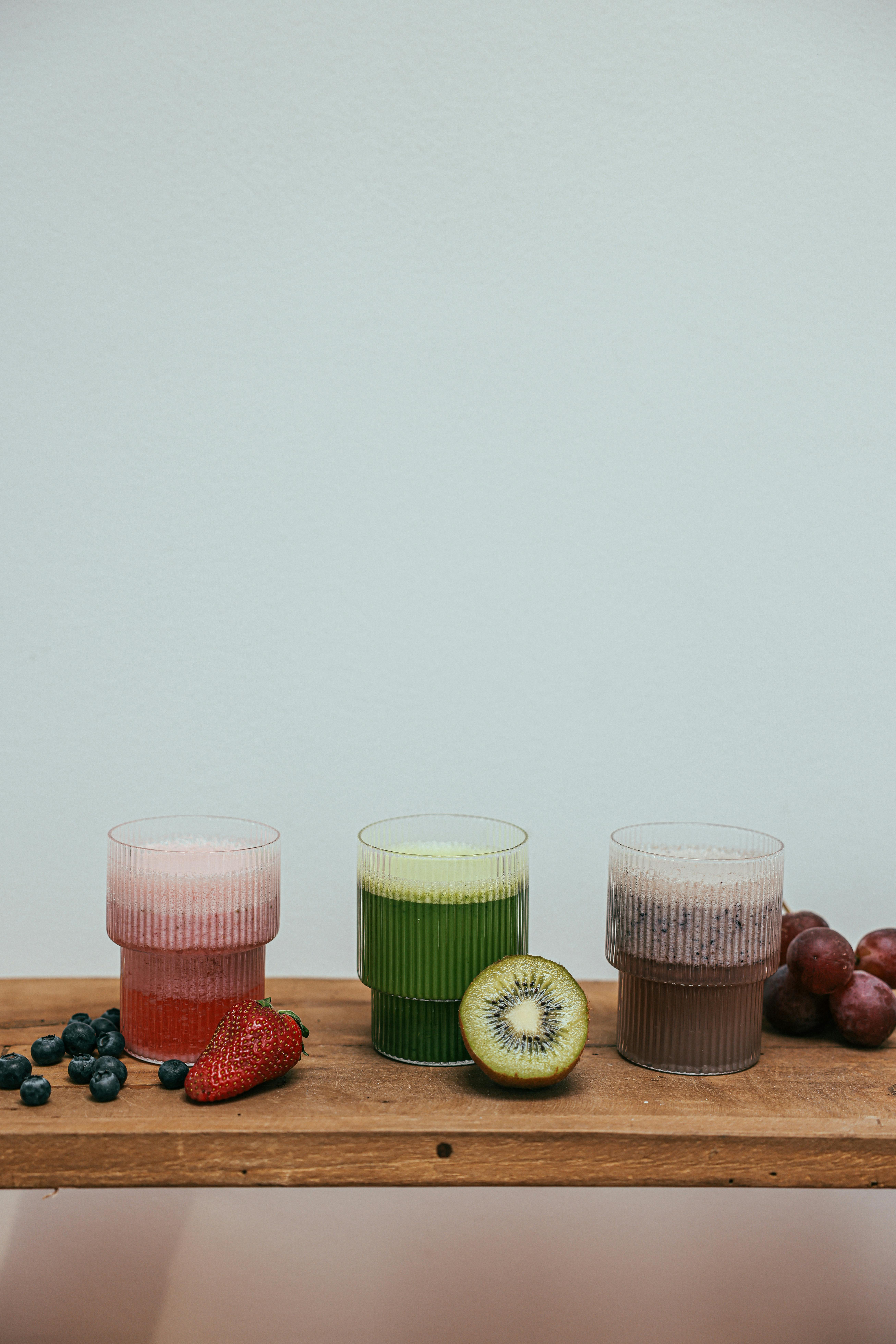 Three vibrant fruit smoothies with fresh fruits on a wooden table, perfect for a healthy lifestyle.