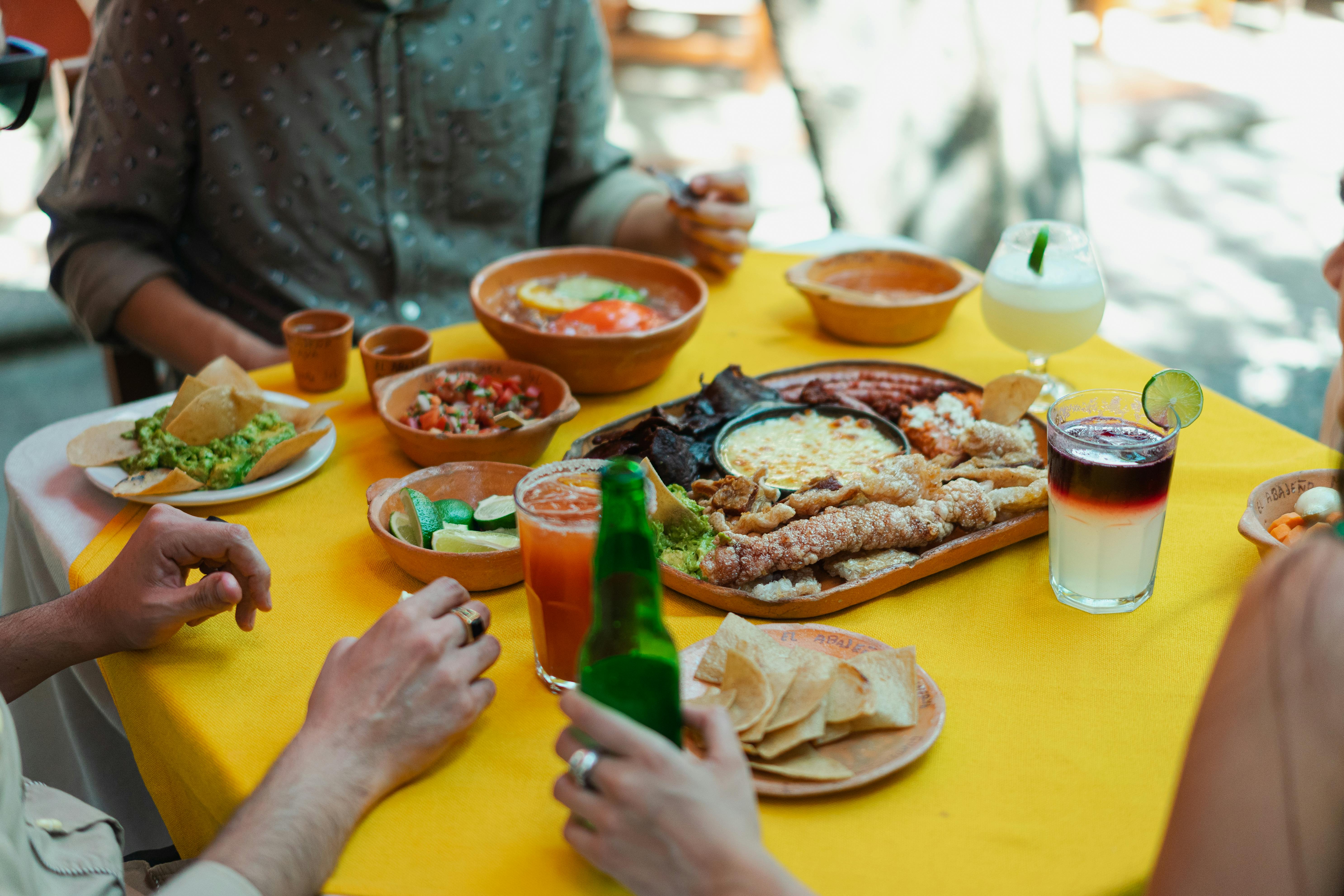 Vibrant scene of Mexican food, drinks, and people enjoying meals outdoors.