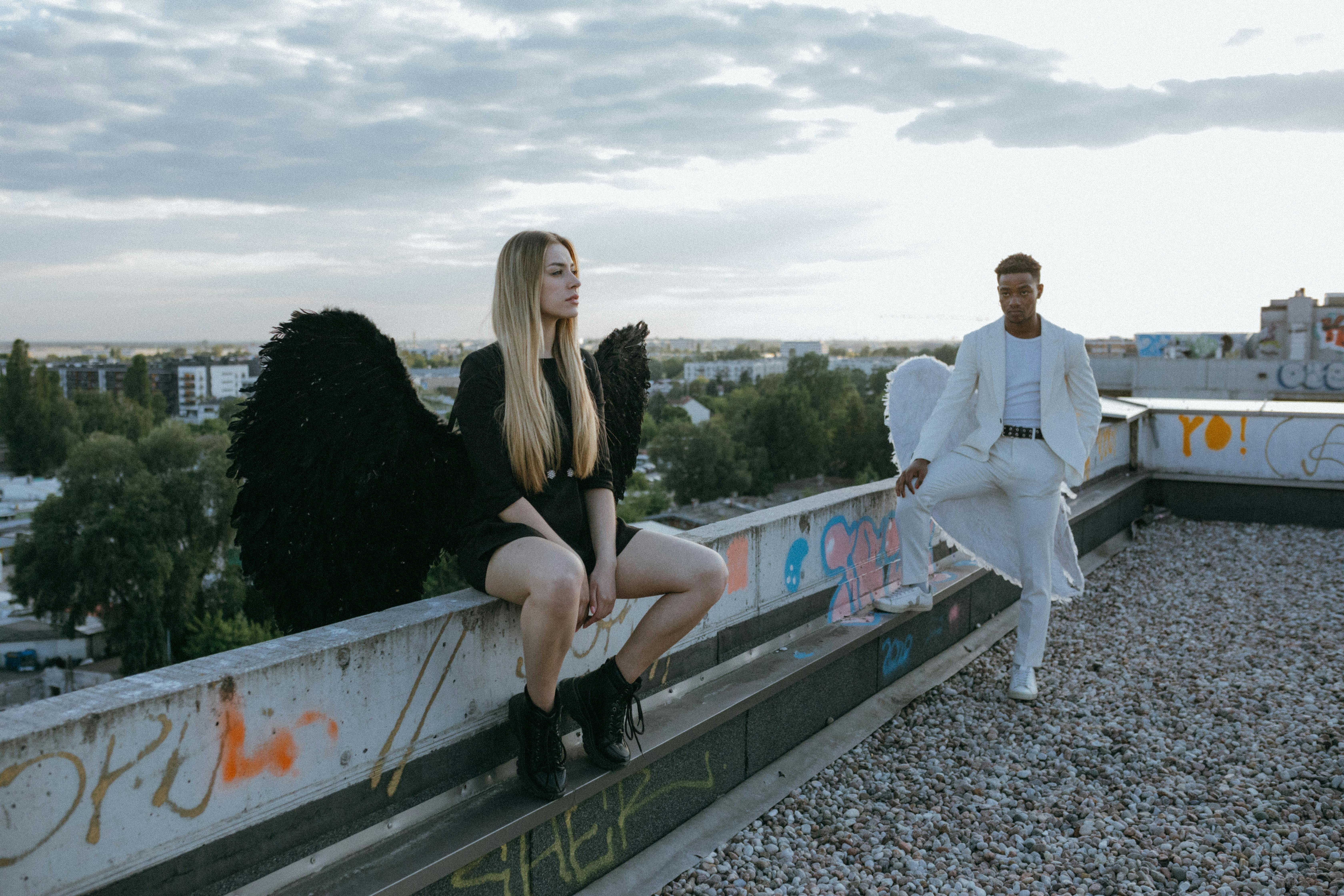 Two figures with wings contrast in black and white on a rooftop.