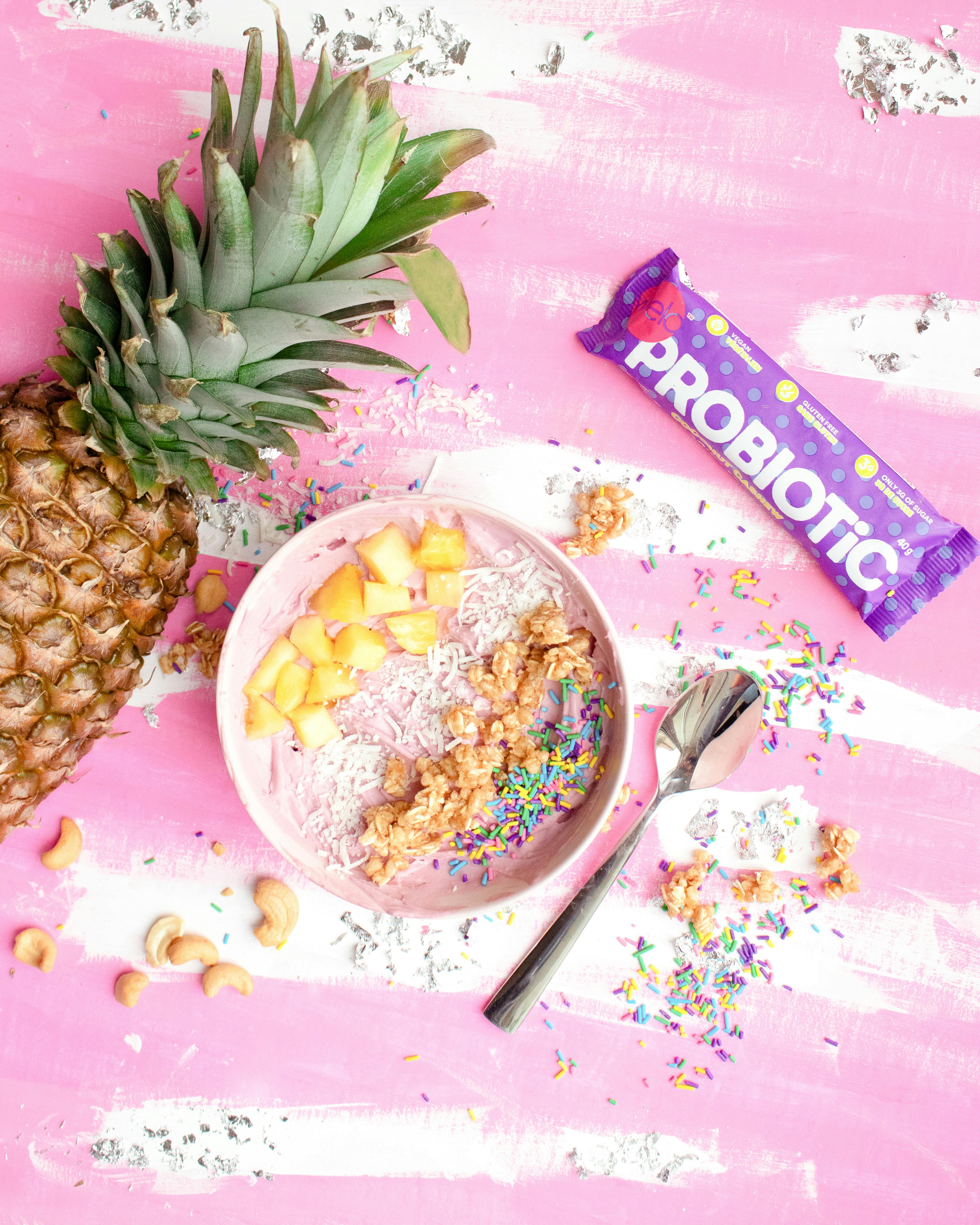 Colorful smoothie bowl with fresh pineapple, probiotics, and sprinkles on a pink background