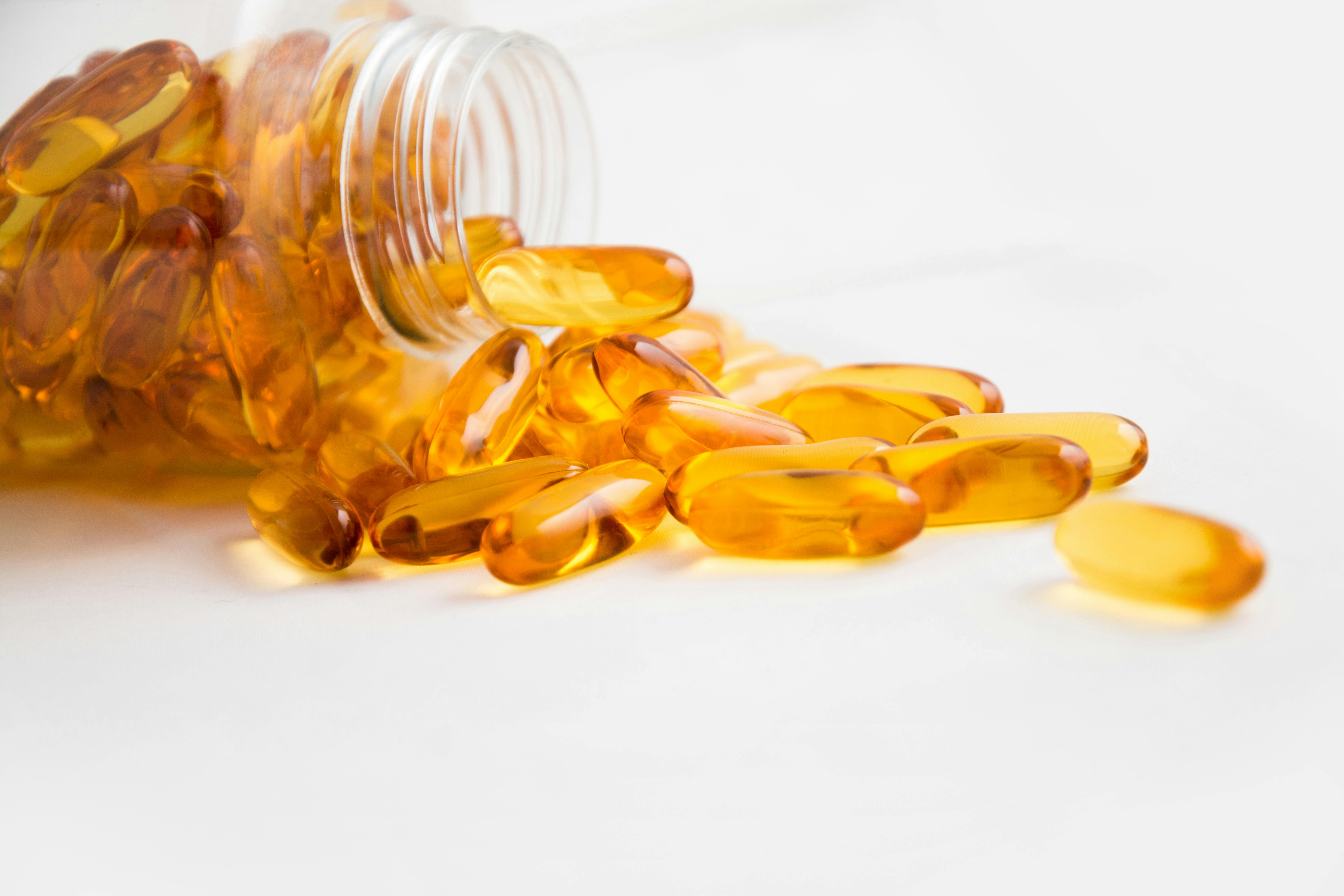 Close-up of fish oil capsules spilling from a bottle on white background