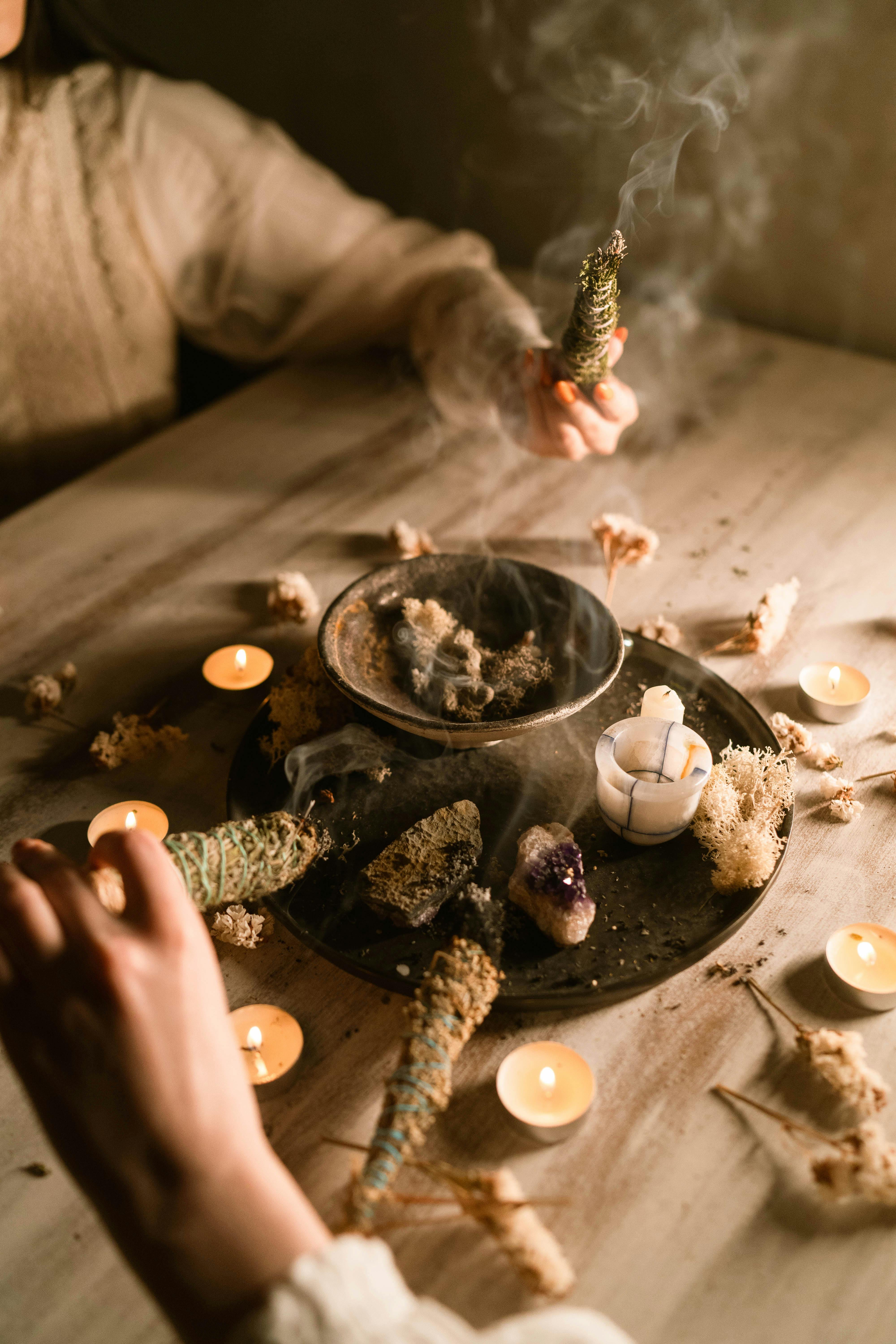 Hands holding sage over a candlelit table with dried flowers, creating a spiritual and serene atmosphere.