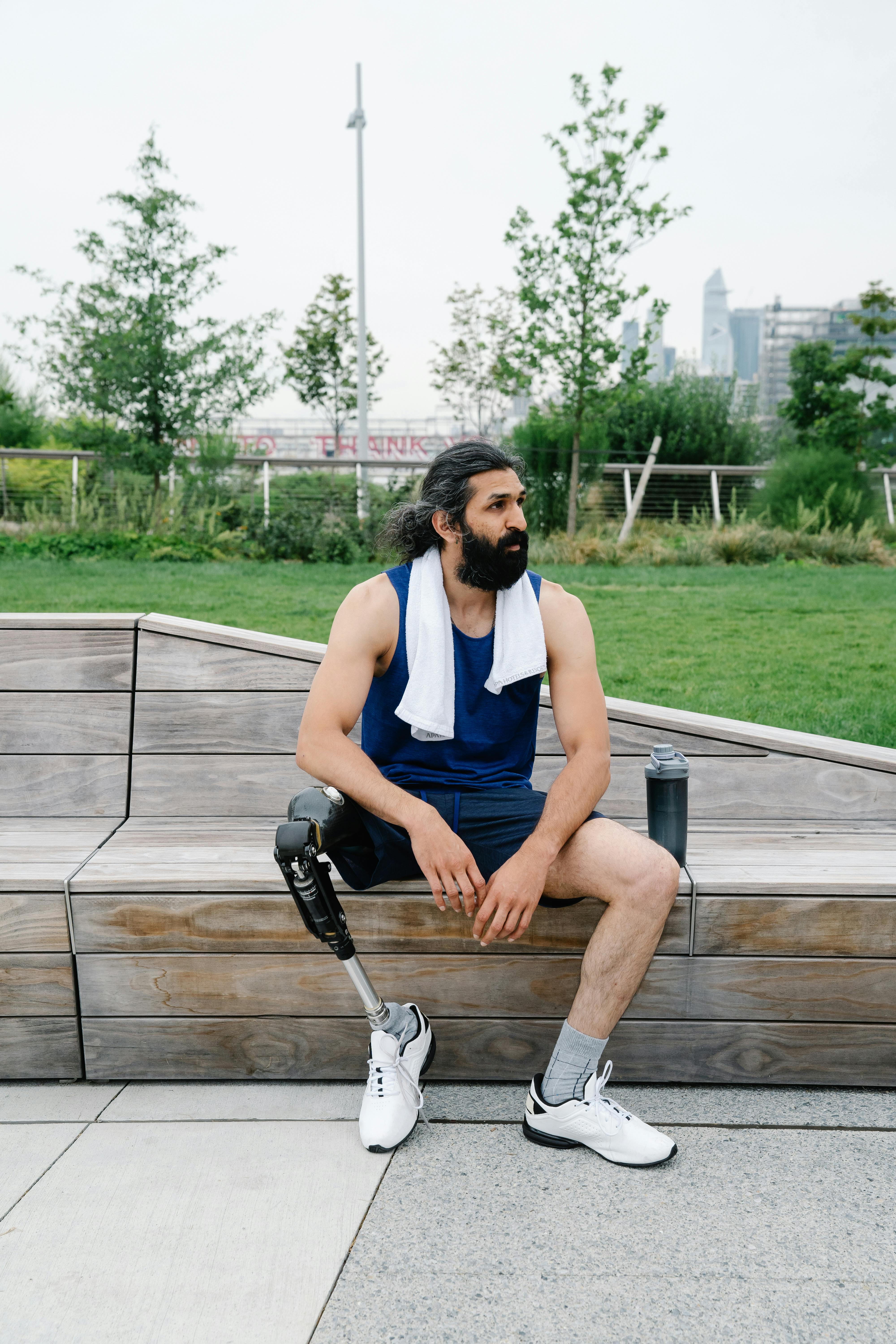 Man with prosthetic leg sitting on a bench outdoors, exhibiting a healthy lifestyle and body positivity.