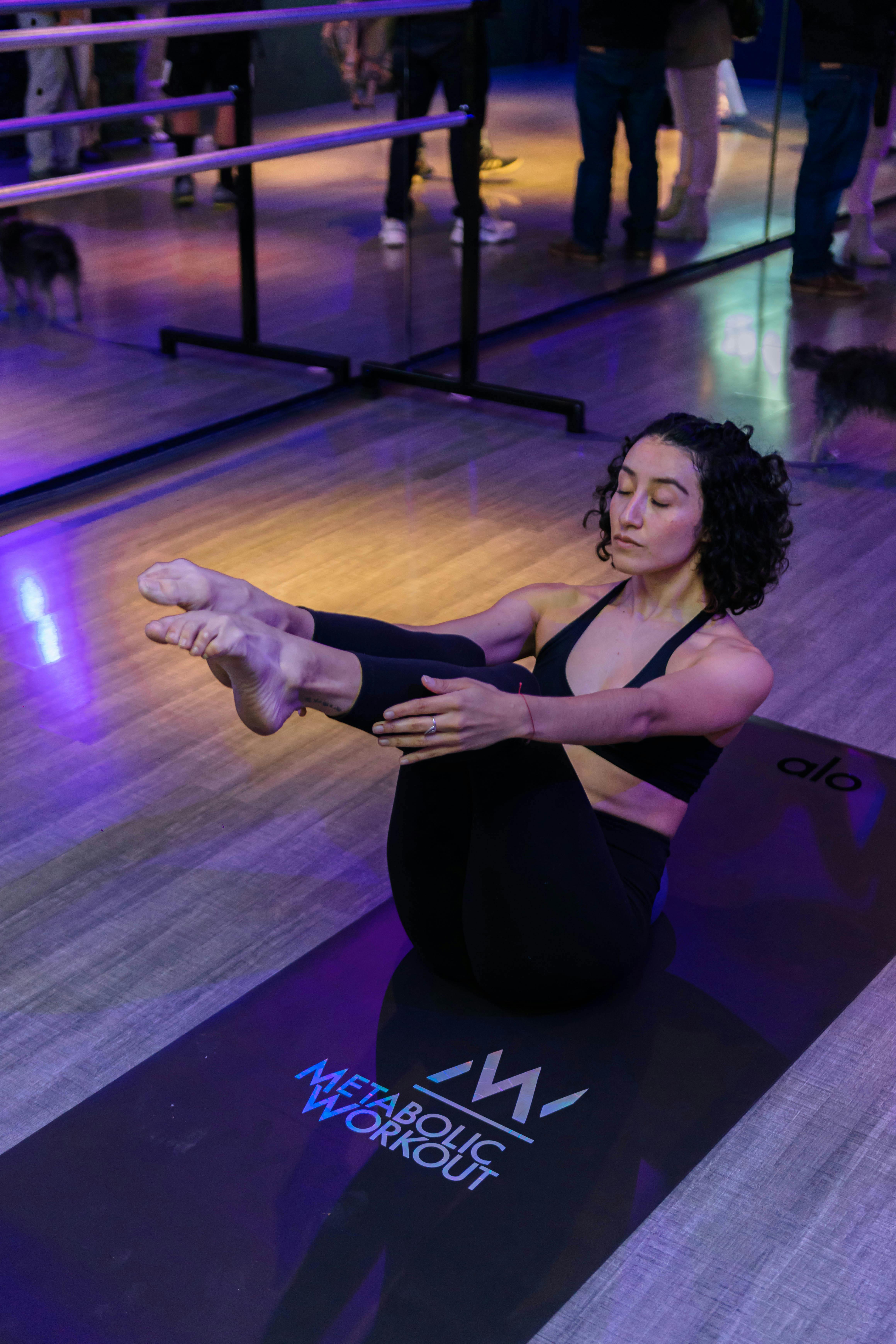Woman in black sportswear practicing yoga on mat in gym. Reflective mirror background adds depth.