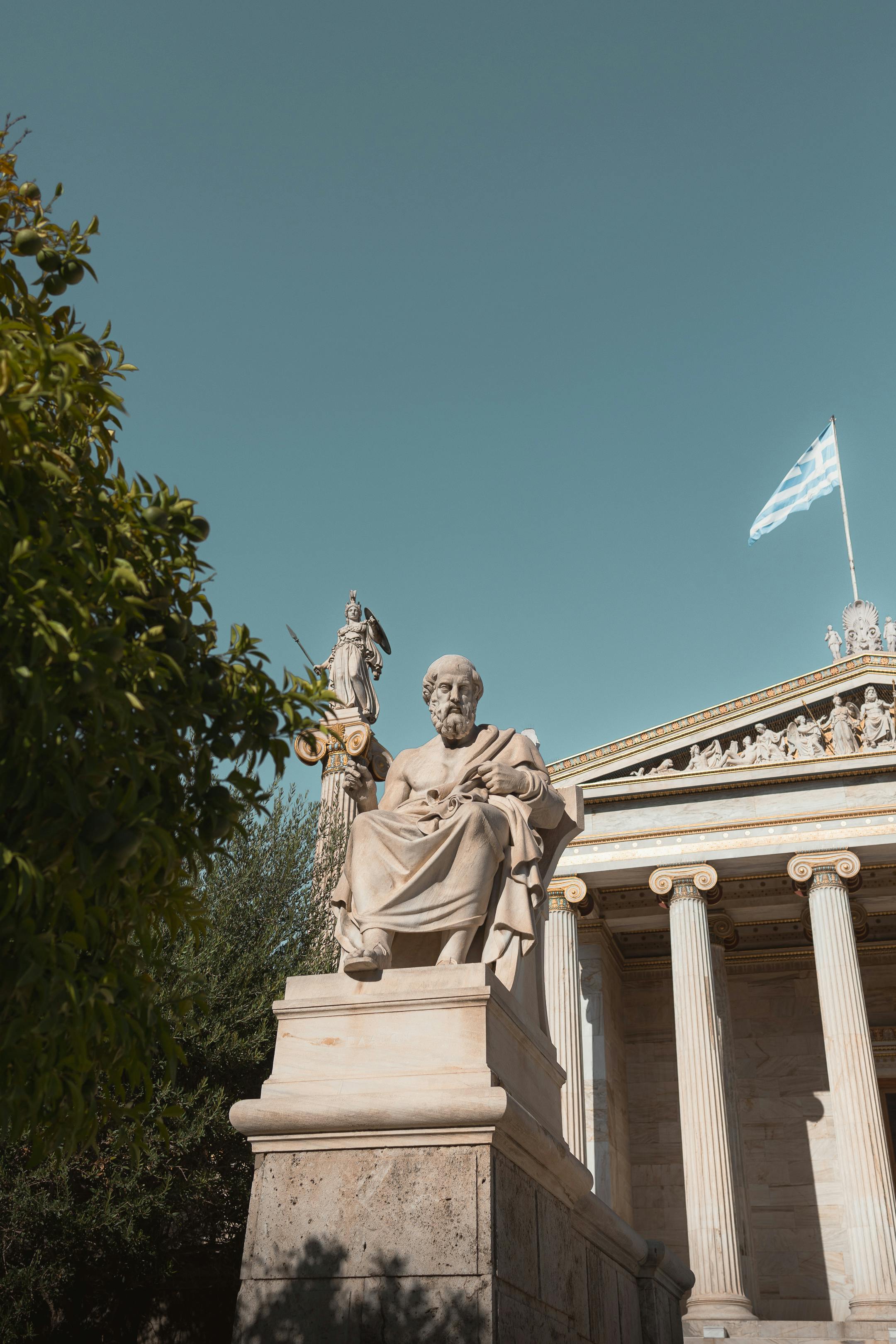 Plato's statue in front of the National Library of Greece against a clear blue sky.