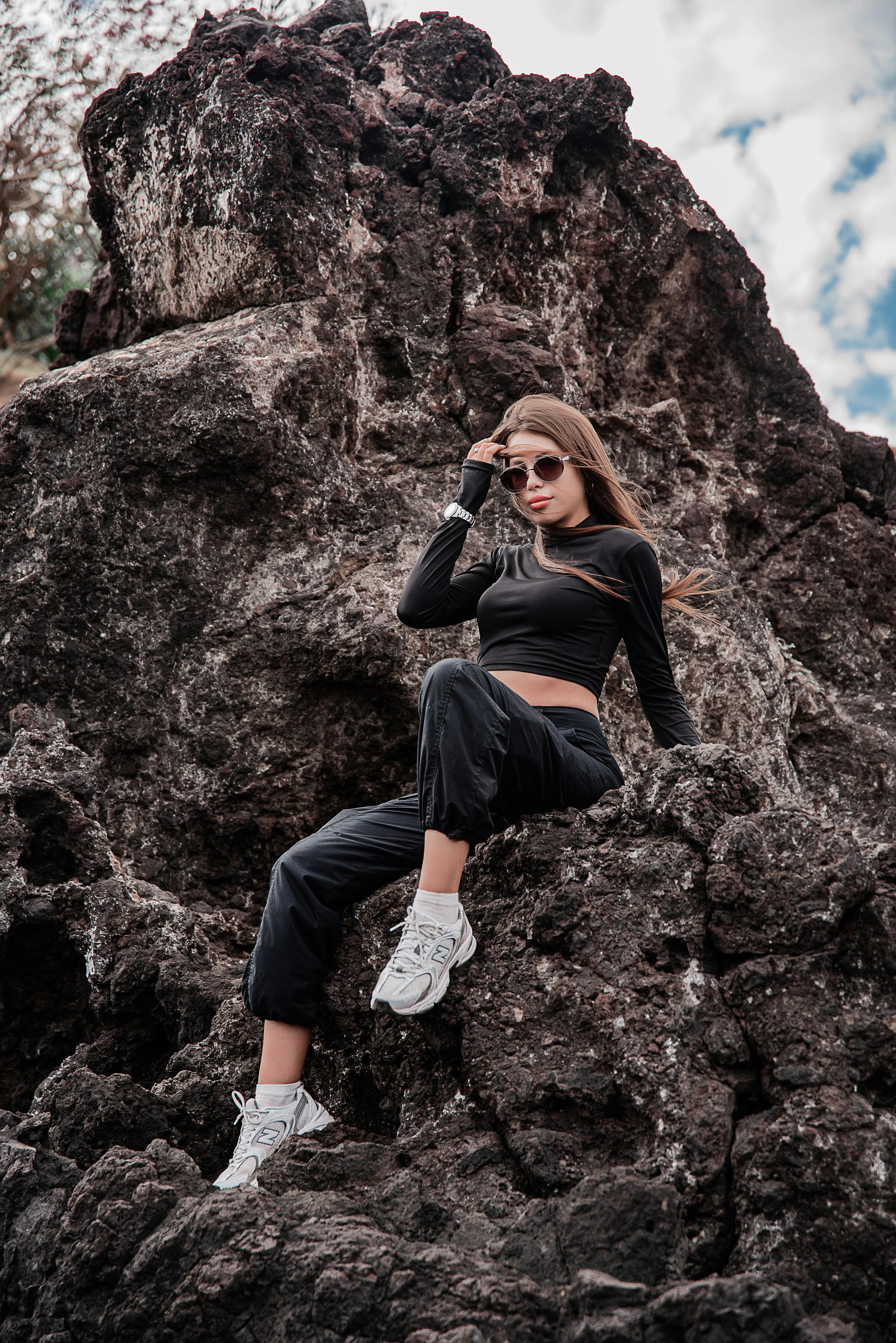 Woman in trendy outfit poses confidently on rocks under a bright sky.