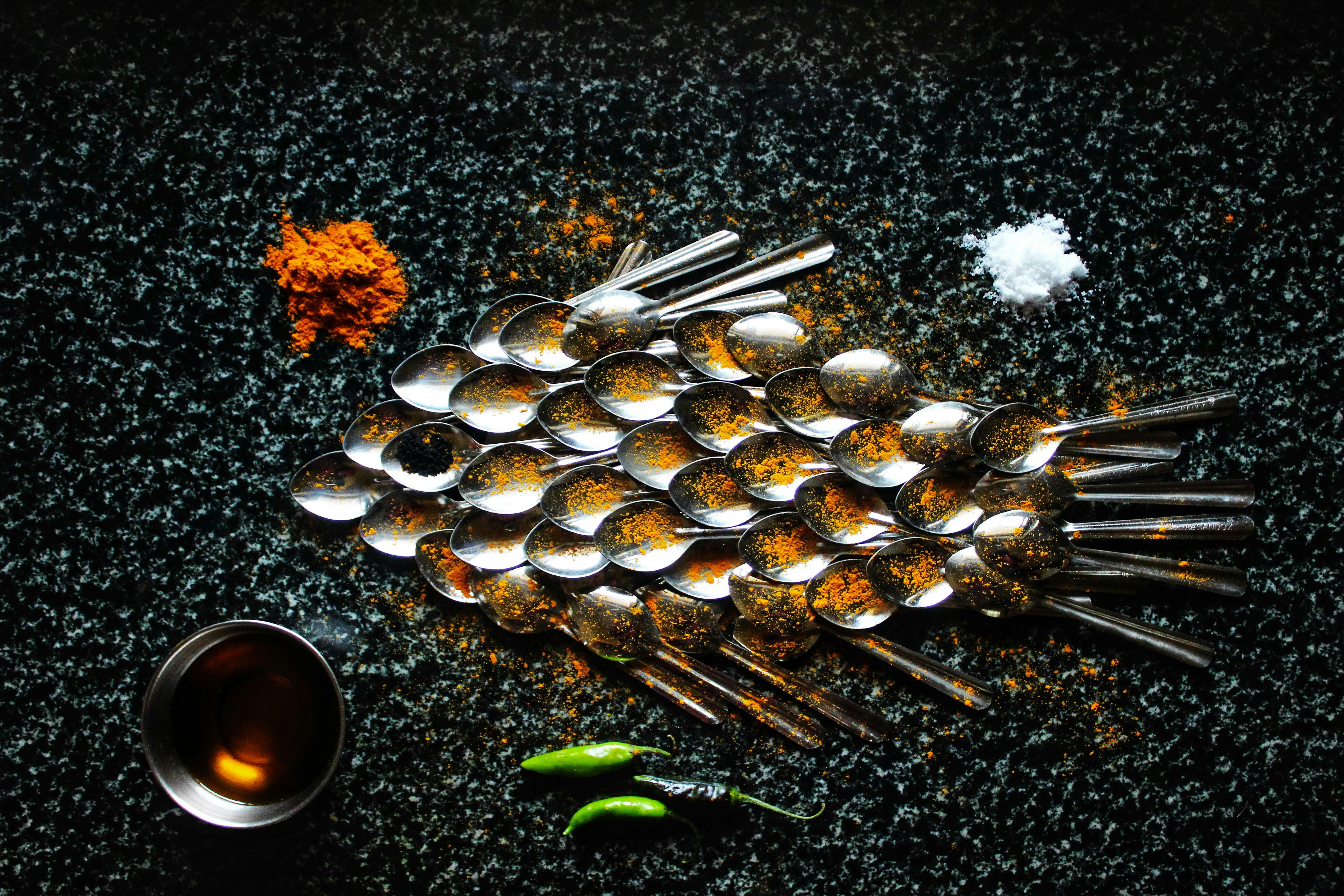 Artistic top view of spoons and spices forming a fish shape on a dark background.