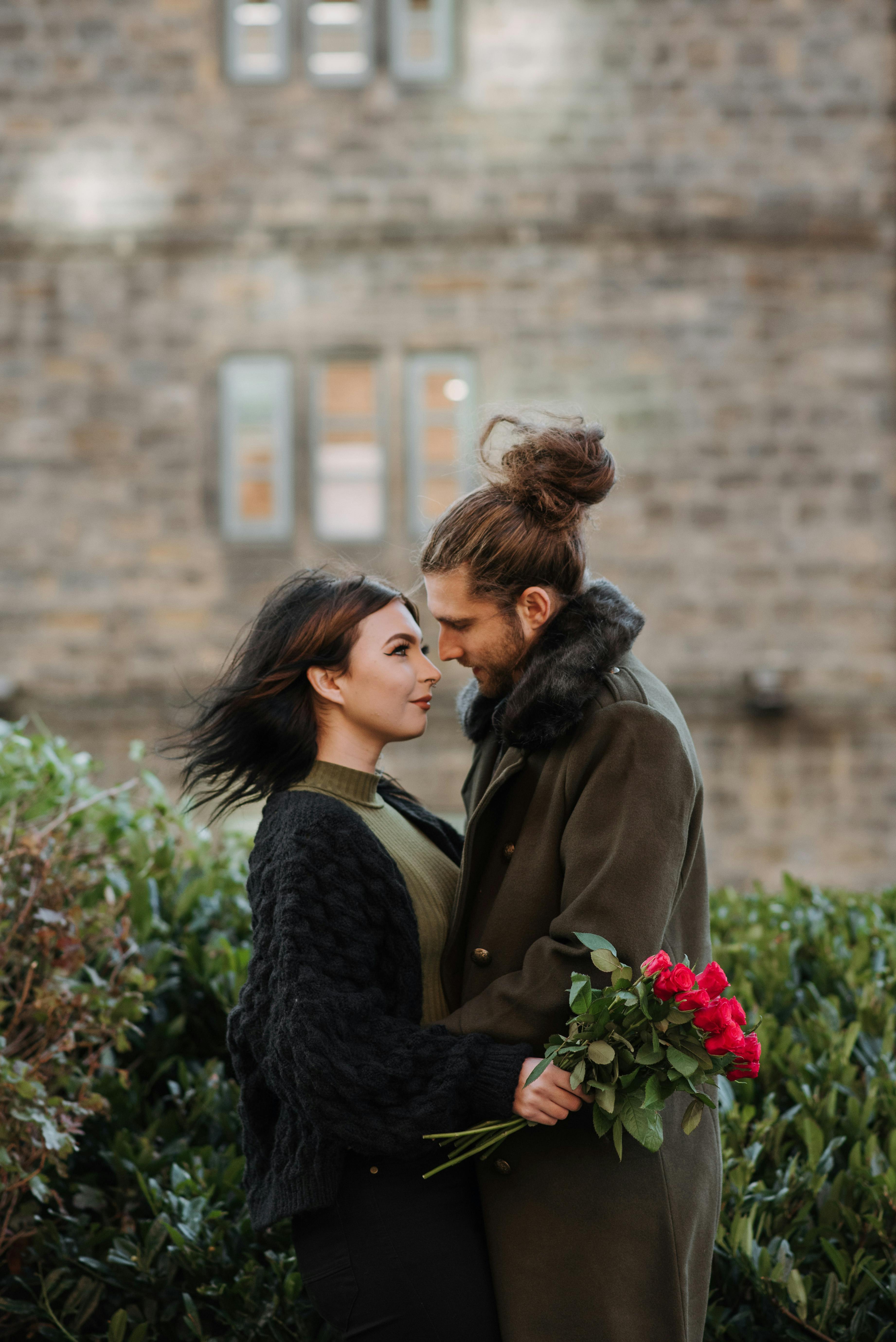 A young couple embraces with roses in a romantic outdoor setting, showcasing love and affection.