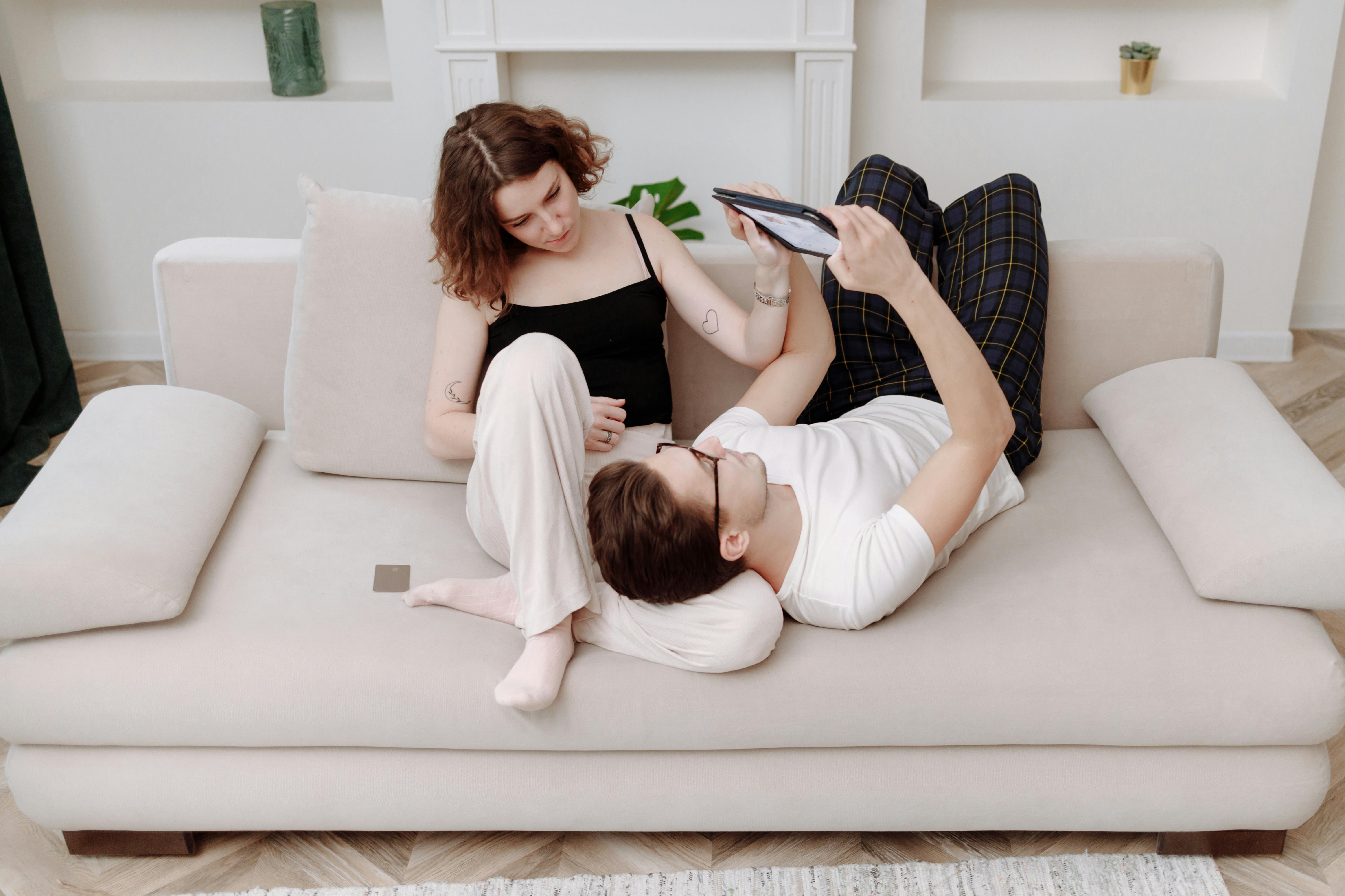 A couple enjoys a leisurely moment on a comfortable sofa, looking at a tablet indoors.