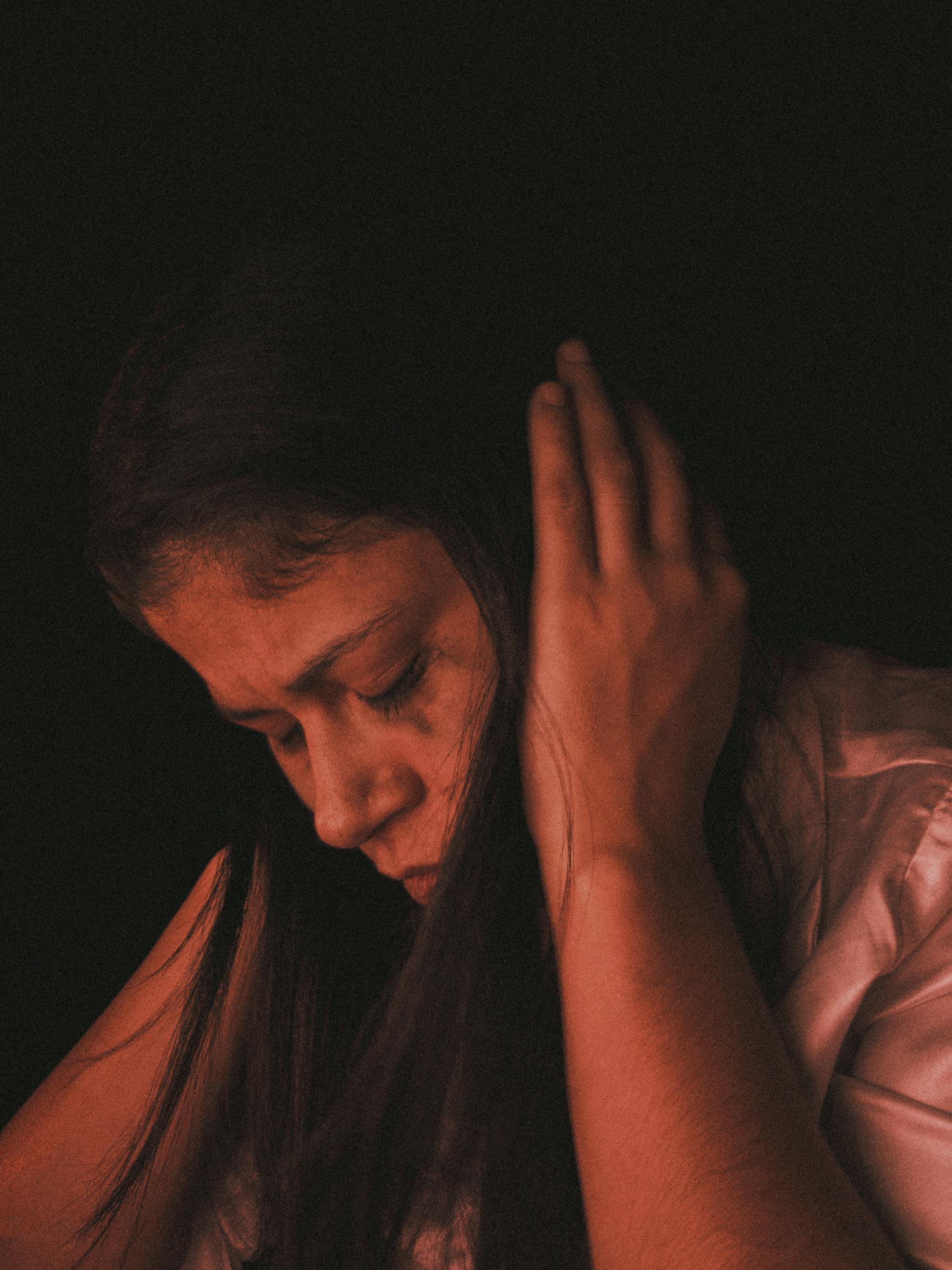 A woman in deep thought, covering ears in a dimly-lit mood, highlighting introspection.