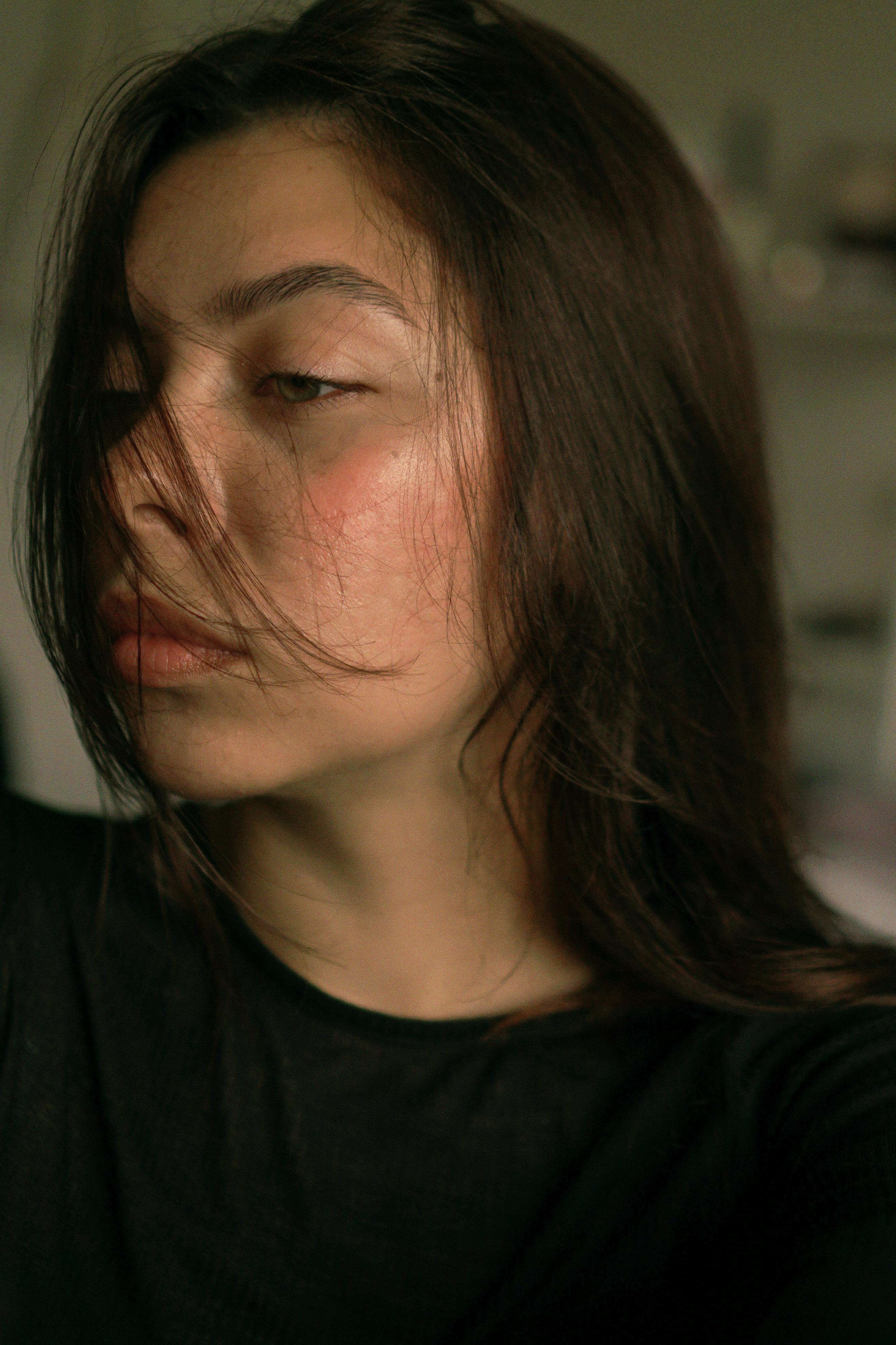 Close-up portrait of a thoughtful woman with windswept hair indoors.