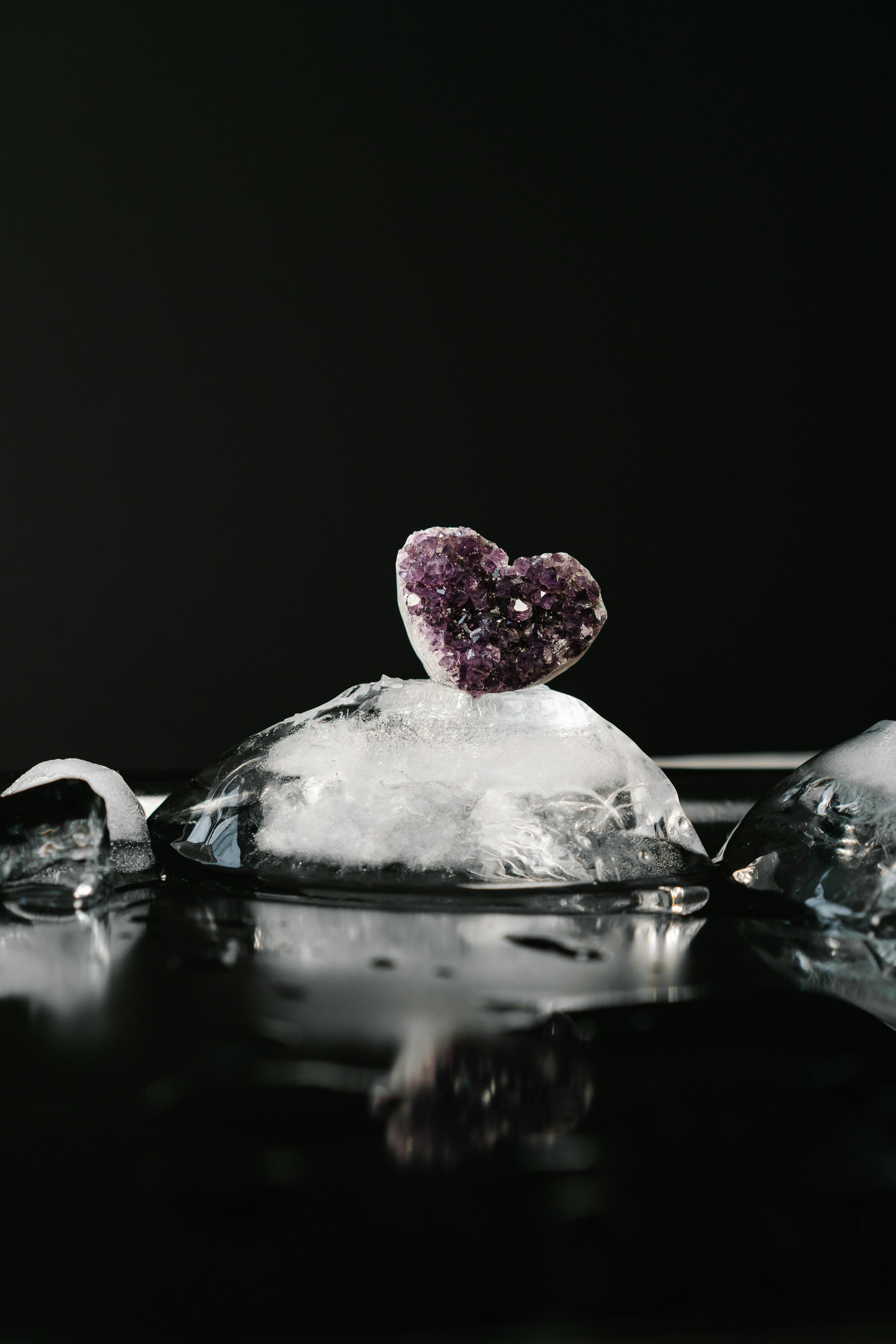 A heart-shaped amethyst crystal atop melting ice against a dark background.