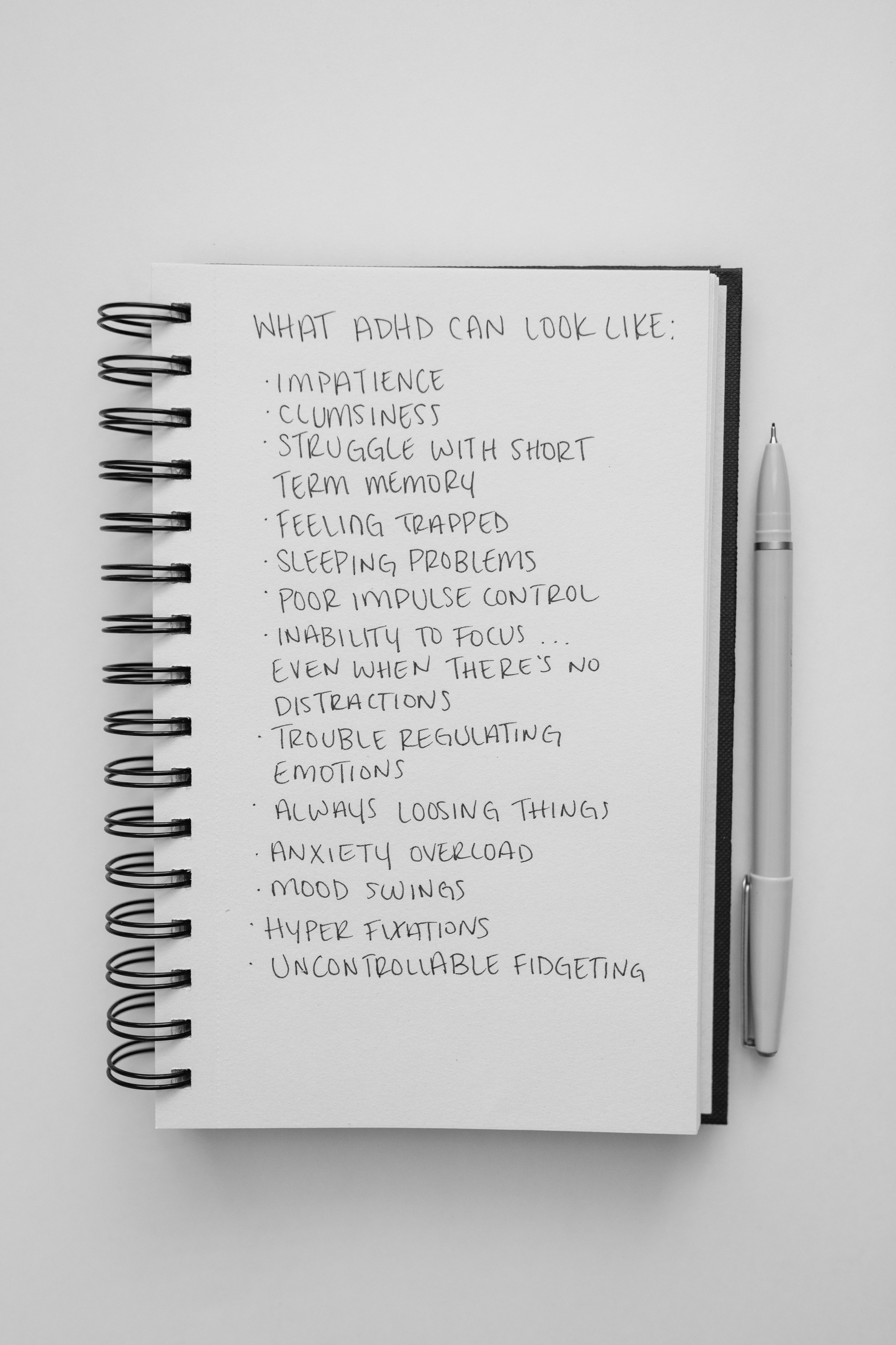 Simple notepad with a list of ADHD symptoms in neat handwriting, accompanied by a pen.