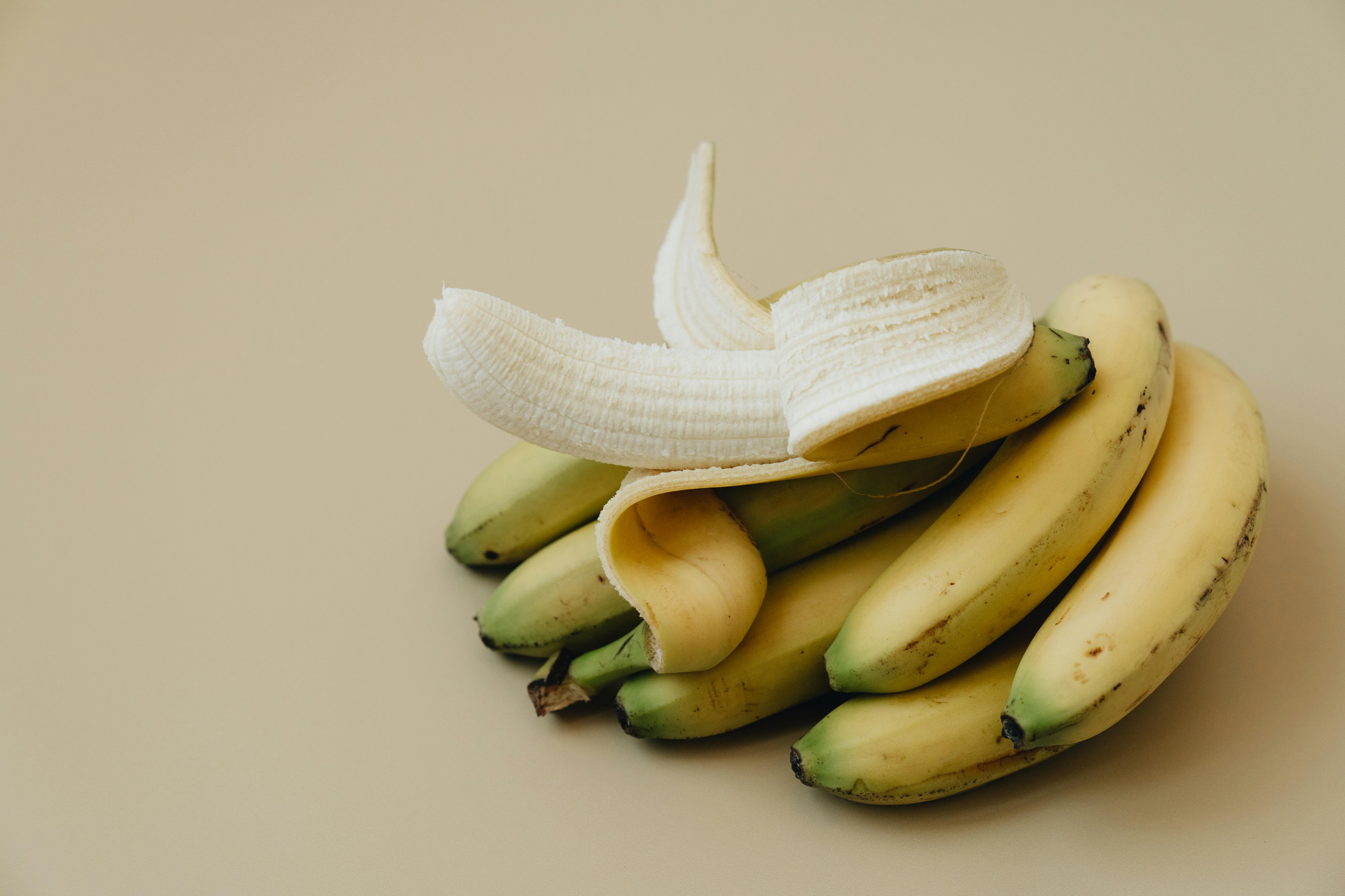 Close-up of a peeled banana on a cluster of fresh bananas, highlighting texture and freshness.