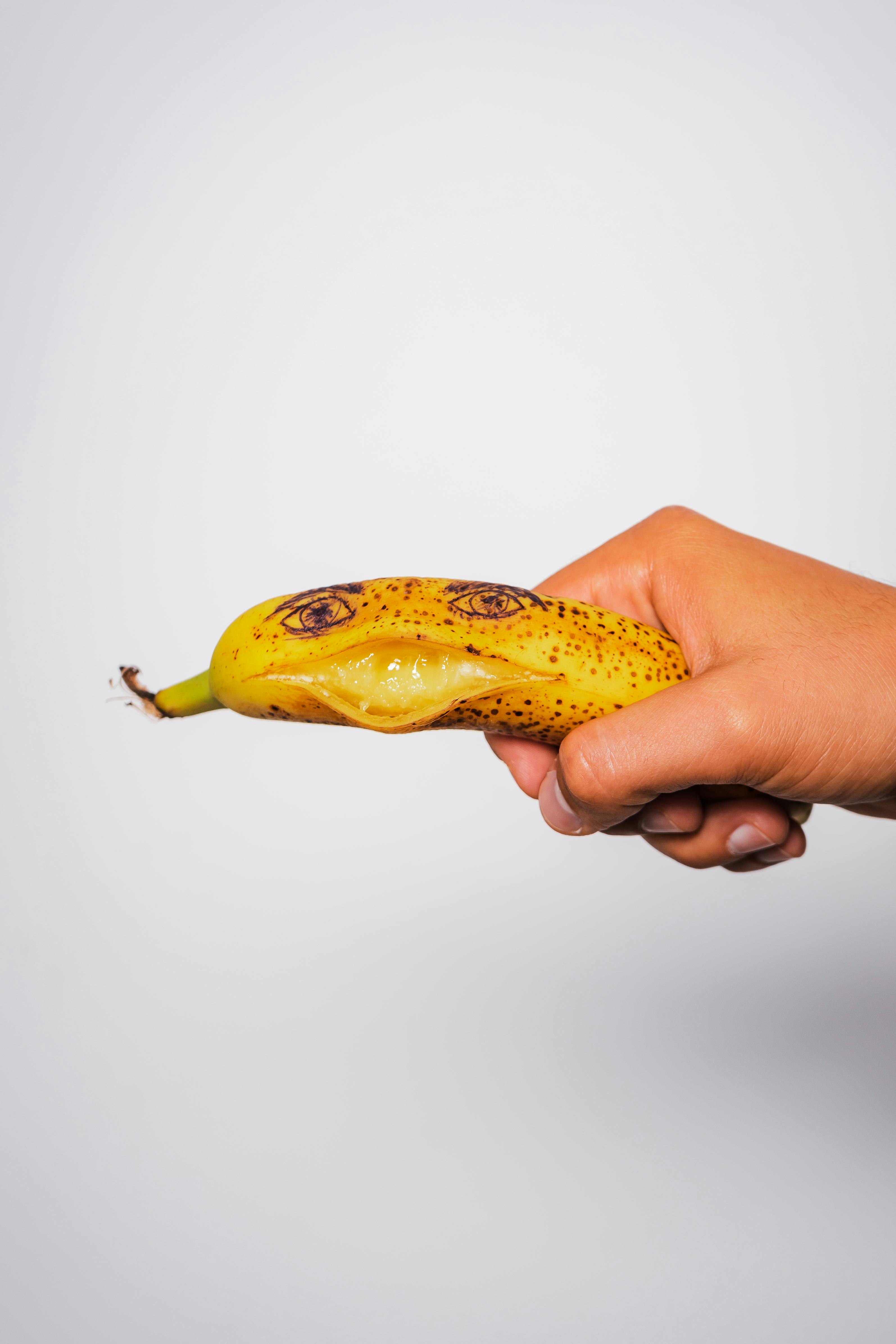 A hand holding a banana with a drawn face on it, showcasing artistic creativity on a white background.