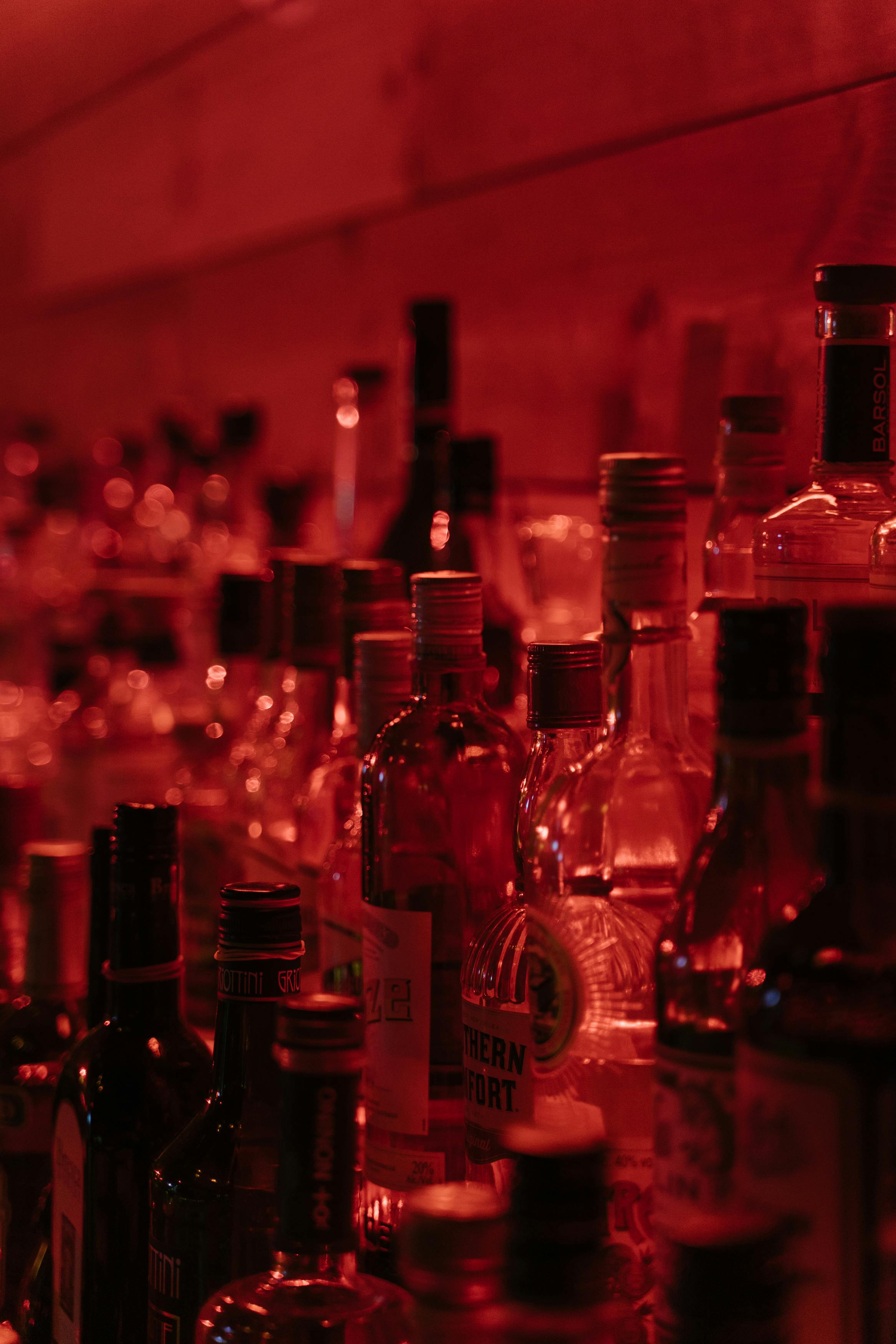 A vibrant array of liquor bottles on a bar shelf set against a warm red ambiance.