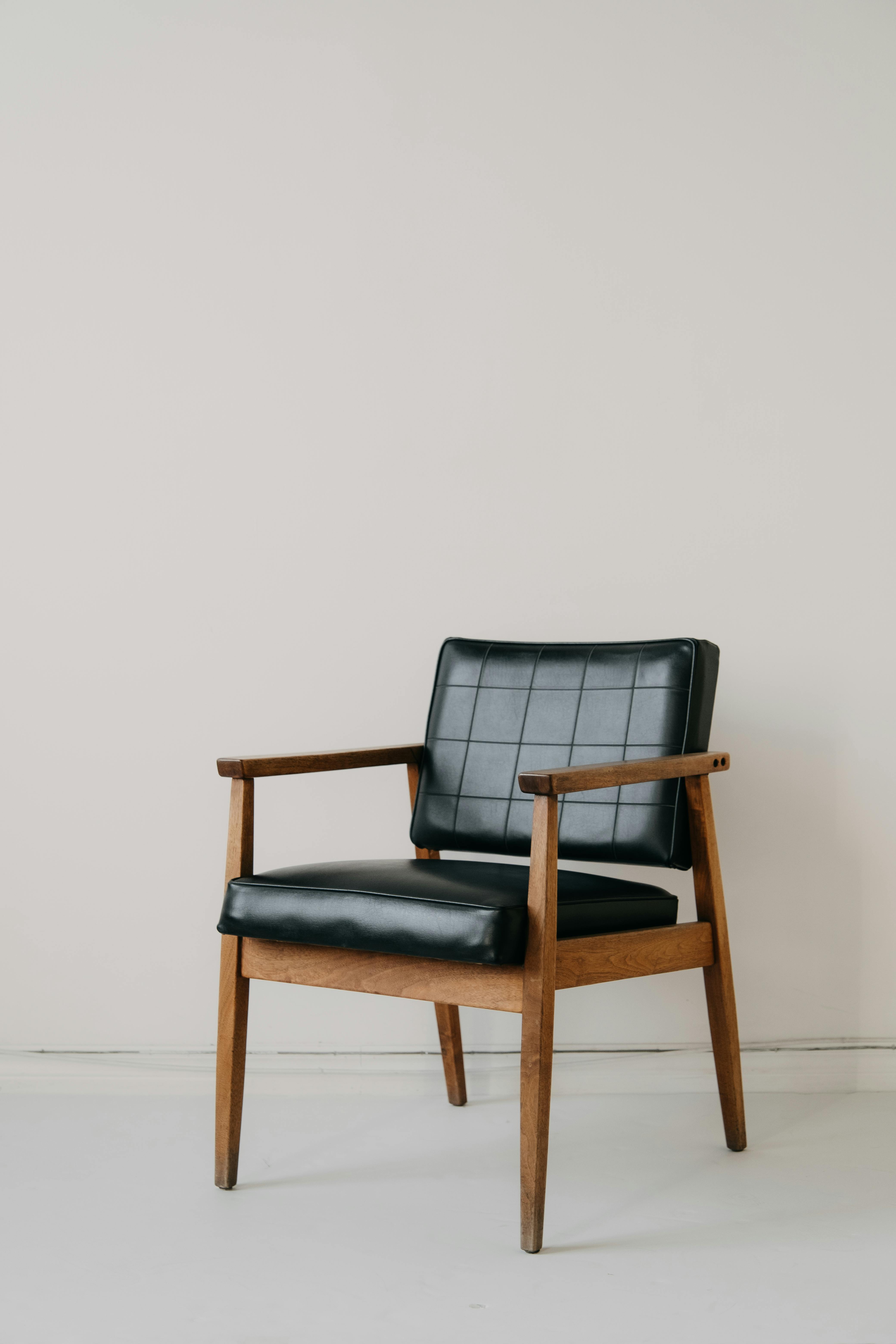 Classic mid-century modern armchair with black leather upholstery on minimalist backdrop, capturing retro style.
