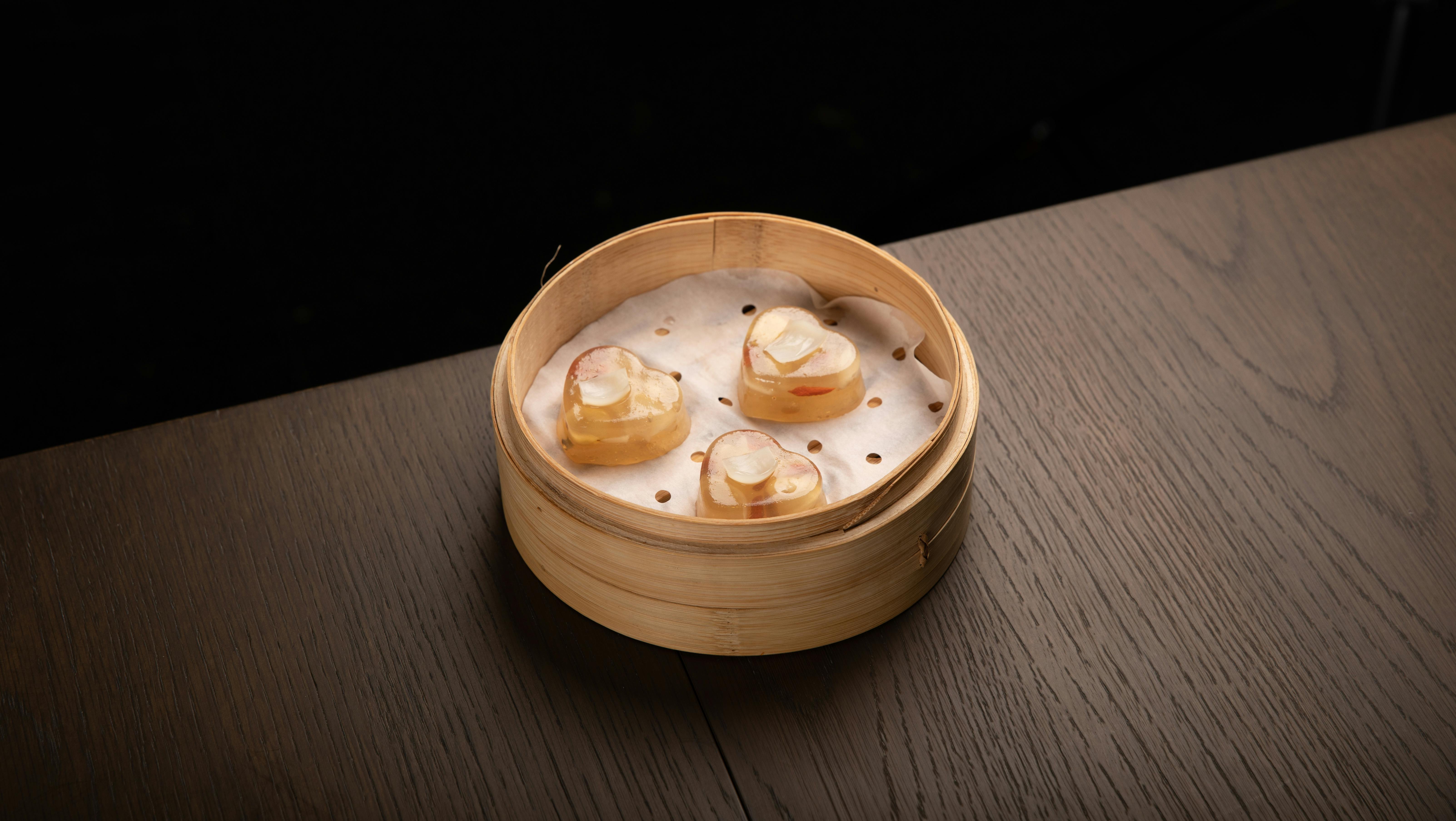 Three heart-shaped dim sum pieces in a bamboo steamer on a wooden table.