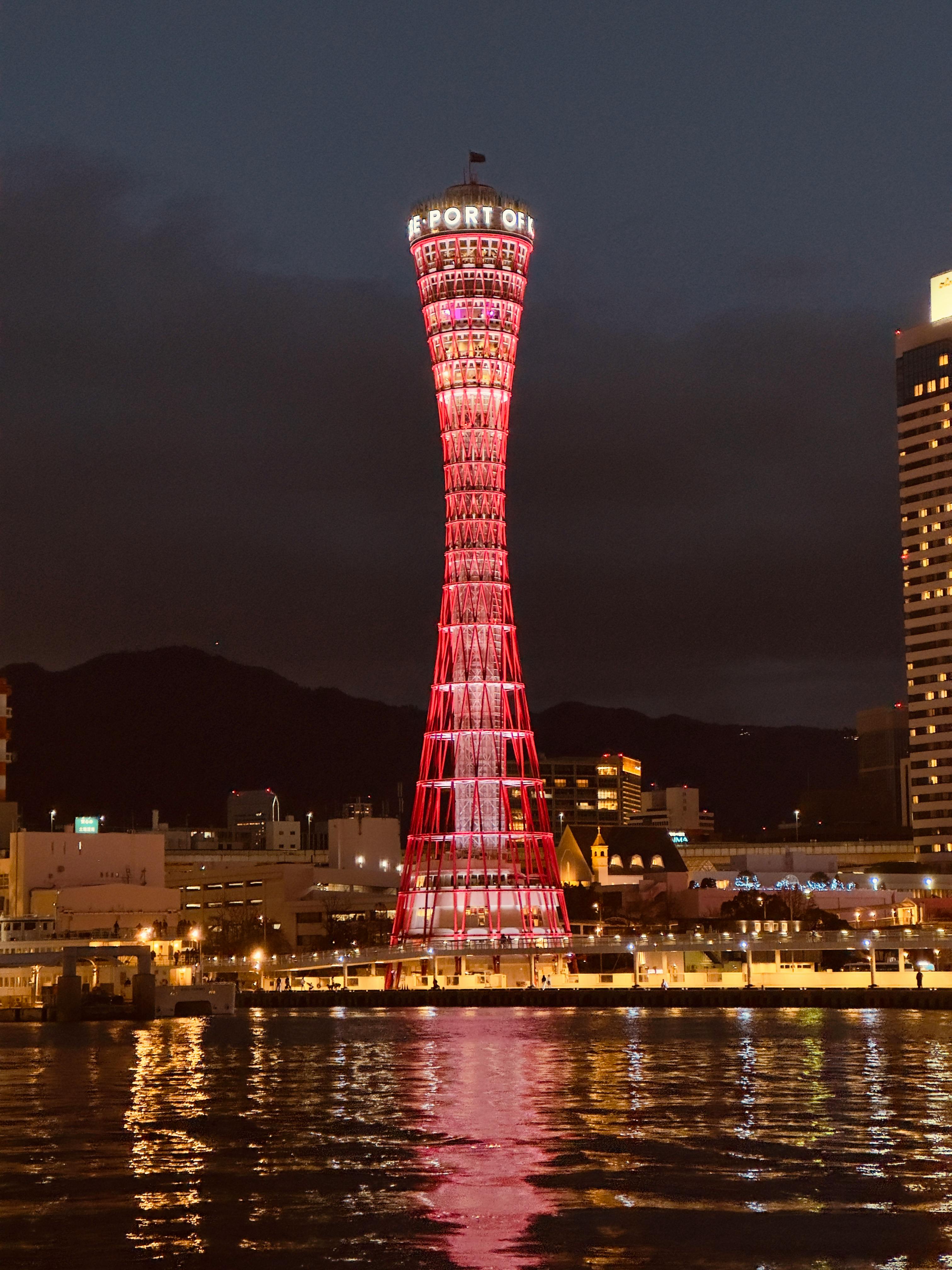 Night view of the illuminated Kobe Port Tower in Japan, reflecting on the water.