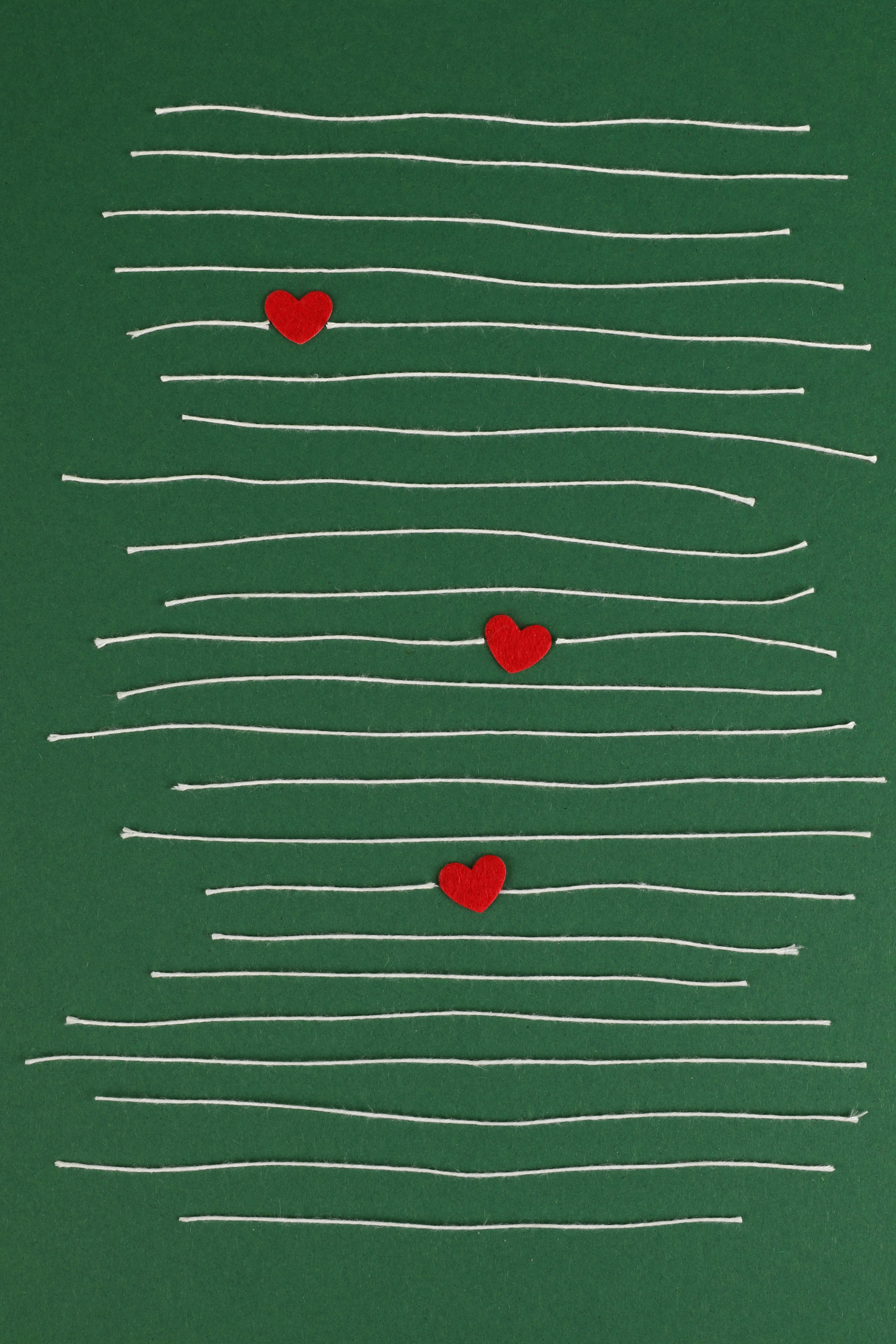 Minimalist art with red hearts on a green background, featuring white string patterns.